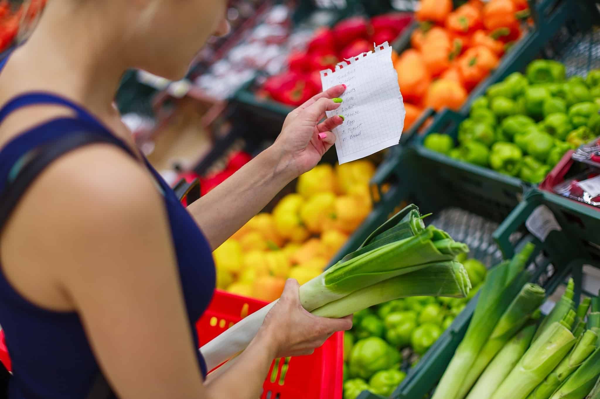 mulher compra legumes no supermercado enquanto agarra em lista em papel