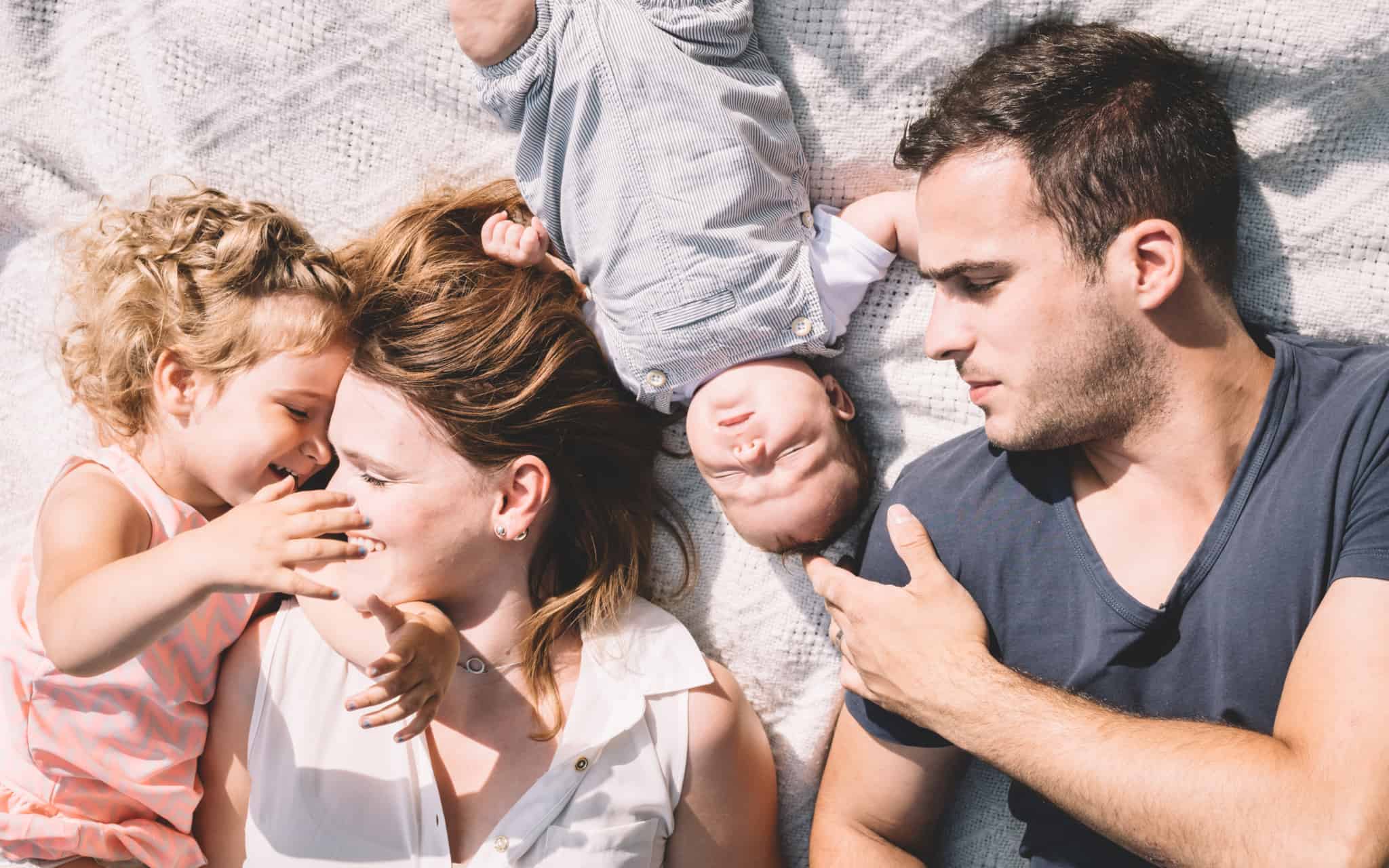 familia com pais uma criança e um bebe deitados na cama