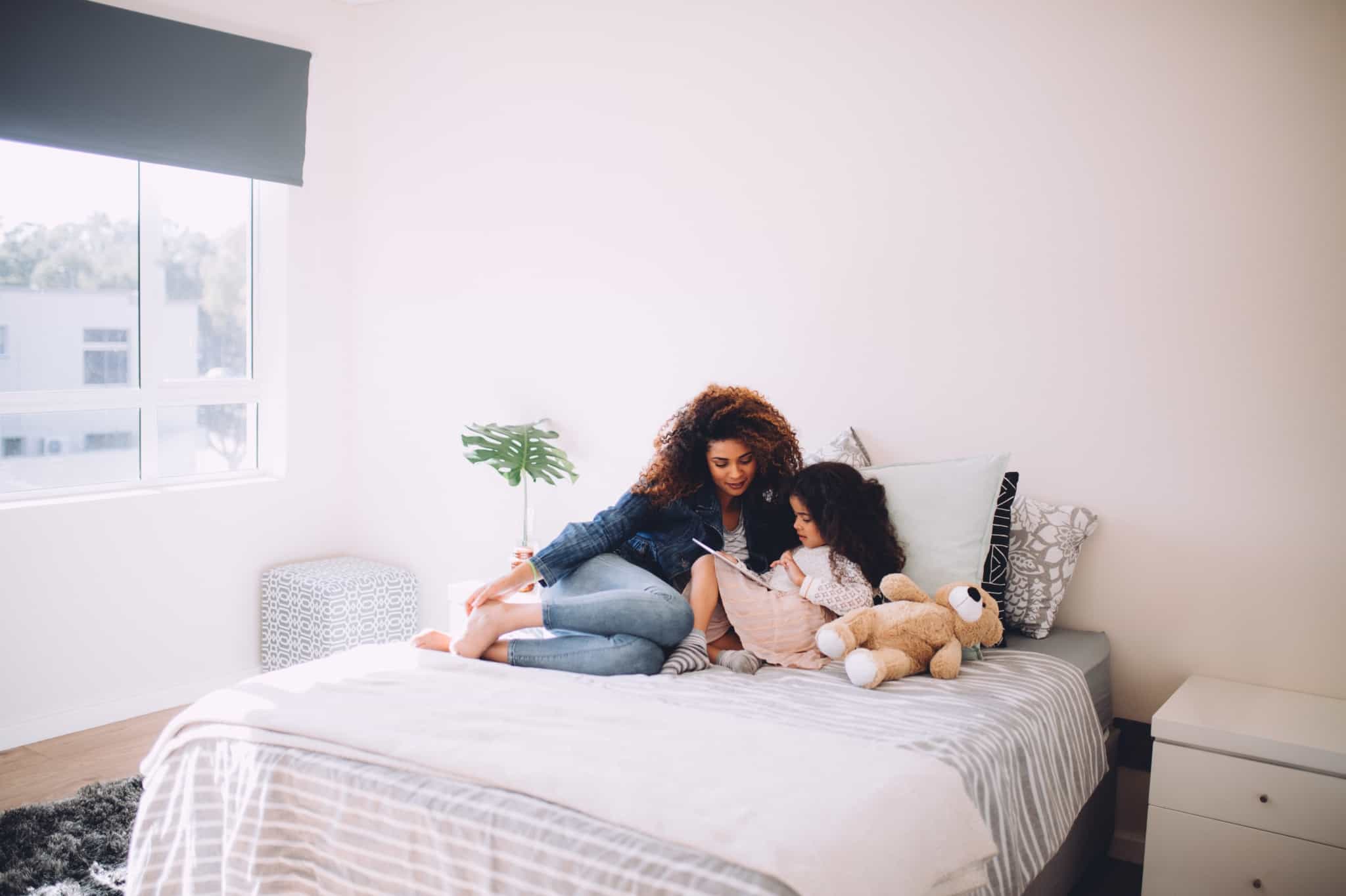 mãe e filha deitadas na cama a ver um livro