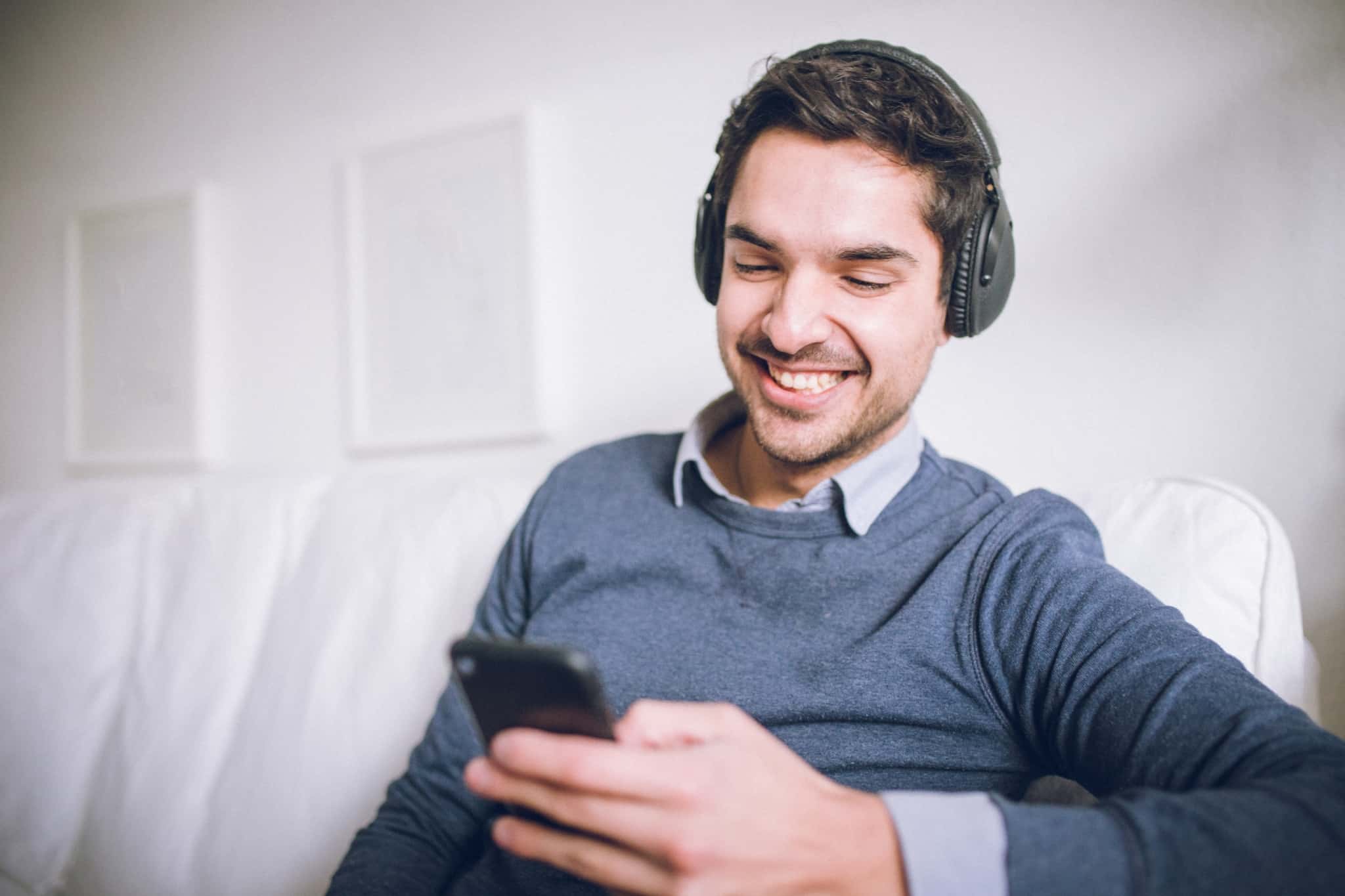 rapaz a sorrir para o telemóvel enquanto ouve com phones