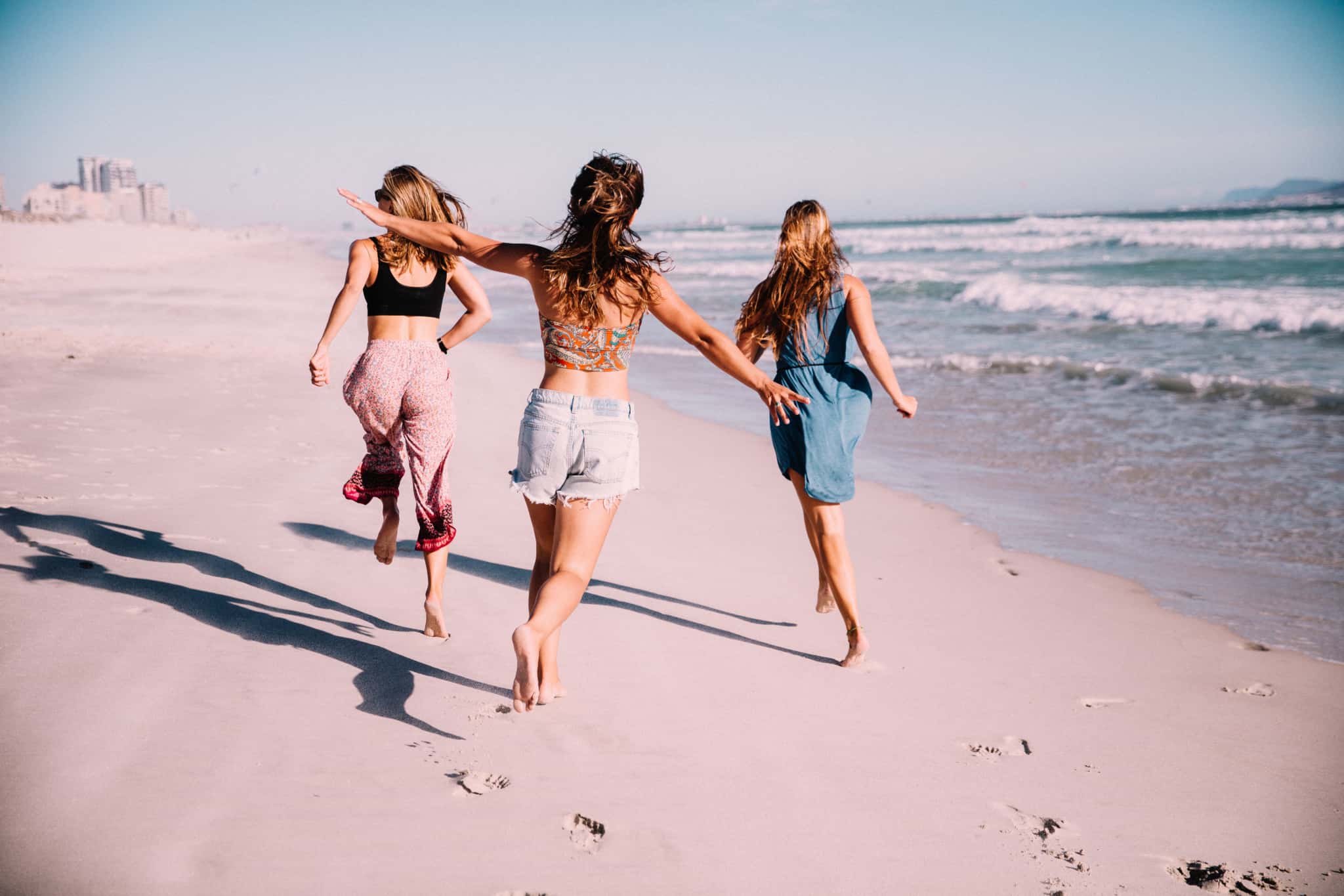 tres raparigas a correr na praia a beira mar