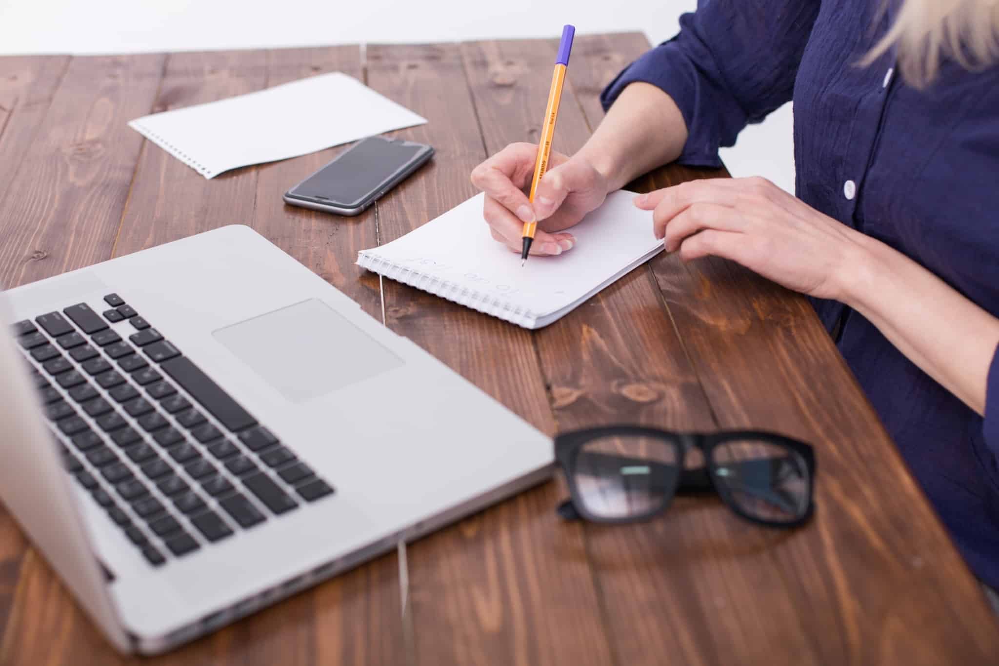pessoa com computador a frente escreve num bloco de notas a lapis