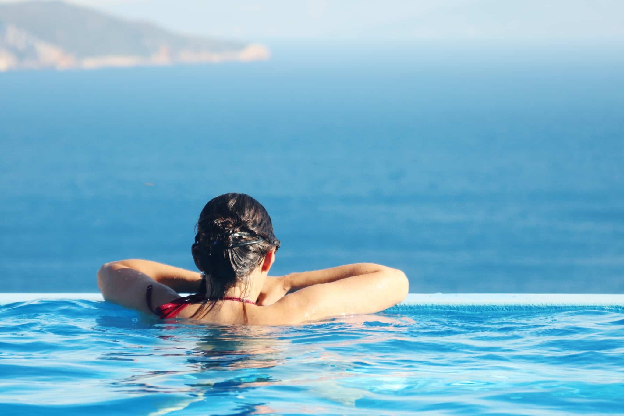 mulher dentro de uma piscina a olhar para o mar