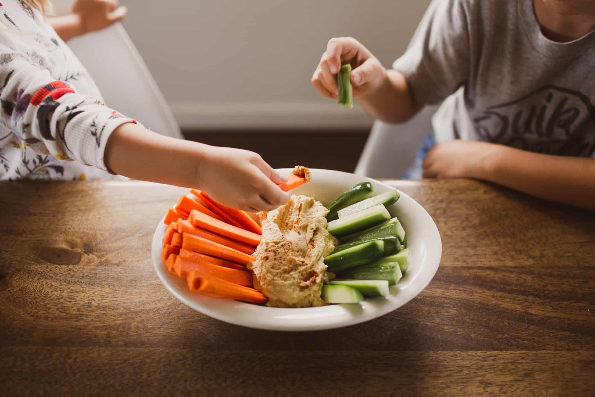 duas crianças a comer humus com legumes