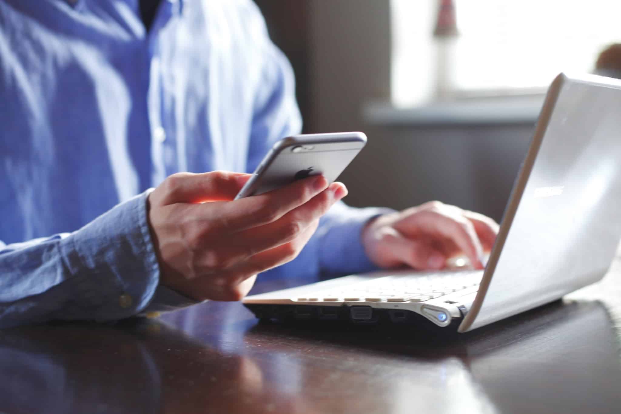 homem a mexer no iphone e no computador portatil