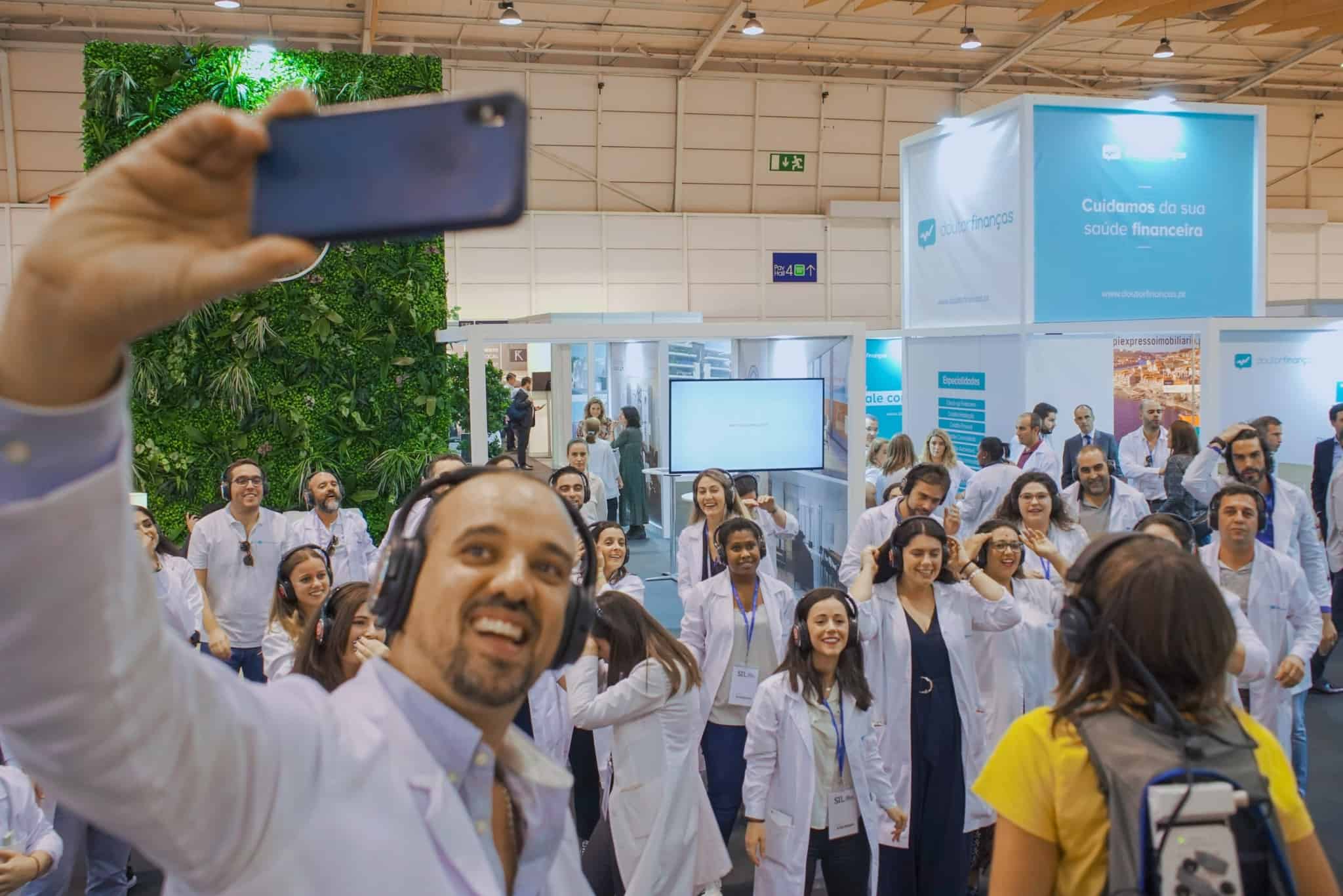 Homem segura telemovel em modo selfie com várias pessoas no background
