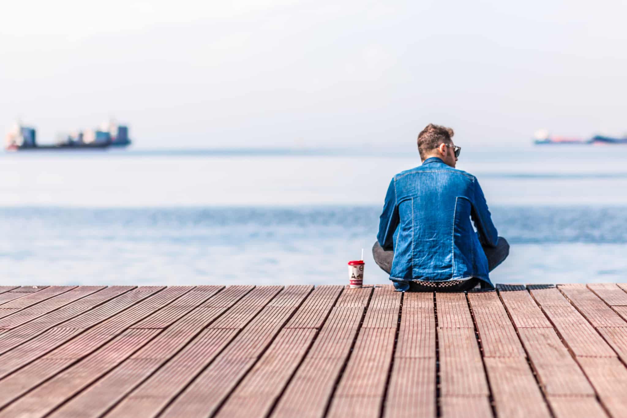 homem a usar ganga a beber café sentado ao pé do mar