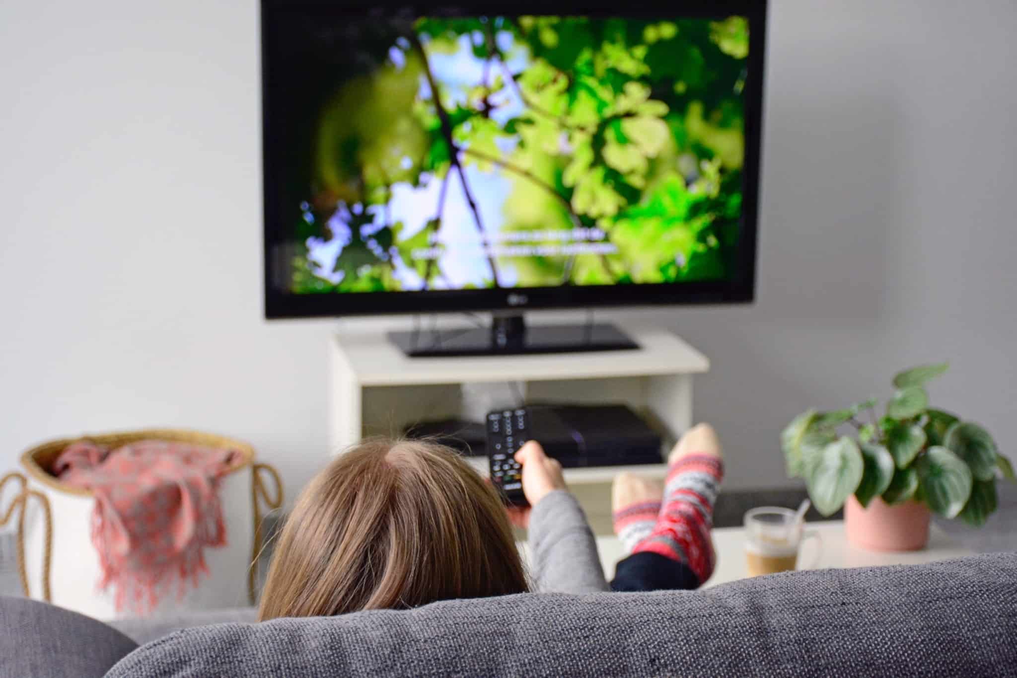 jovem rapariga no sofá com o comando na mão a ver televisão