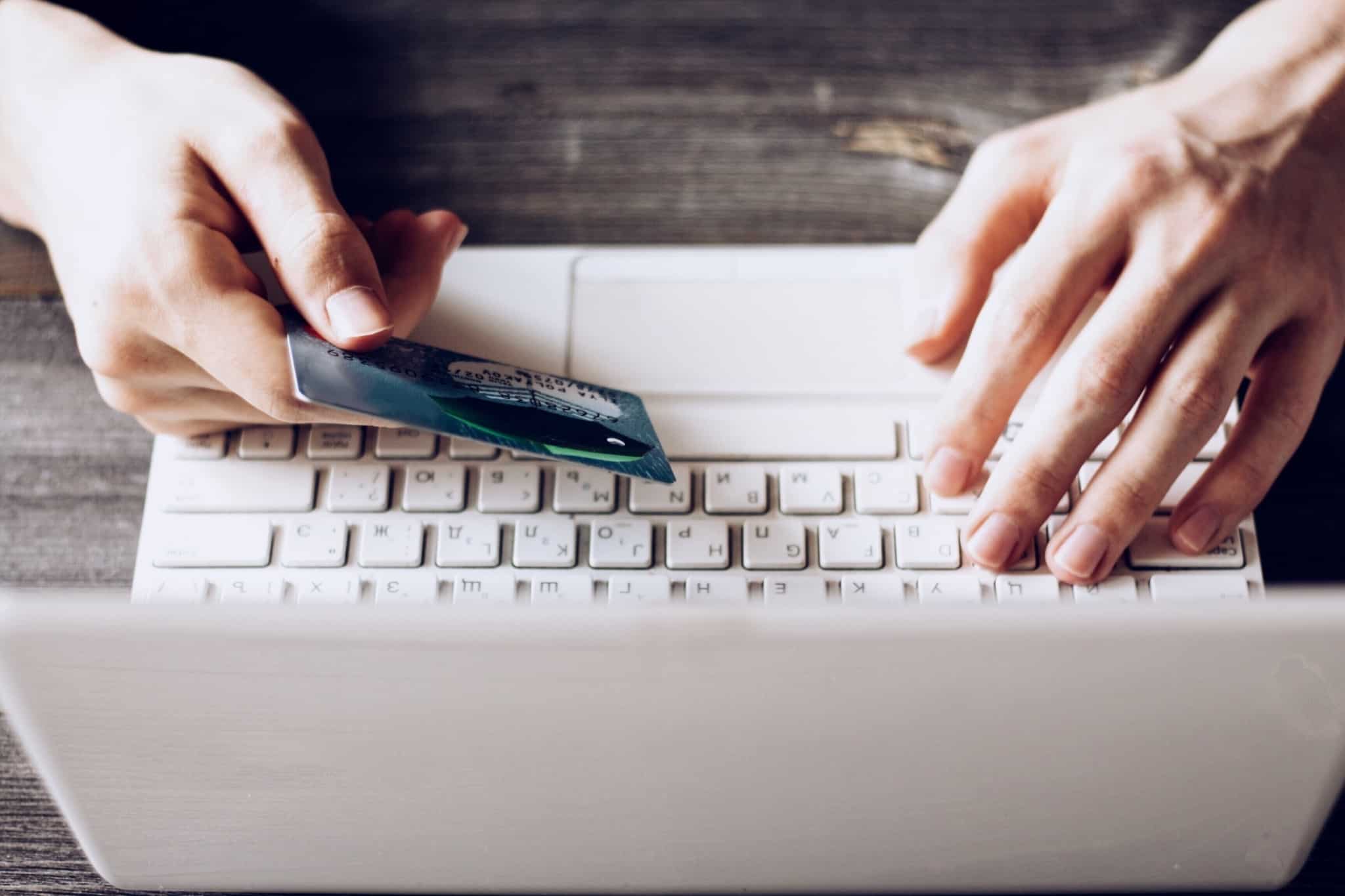 pessoa com o portatil branco e o cartão de crédito na mão direita