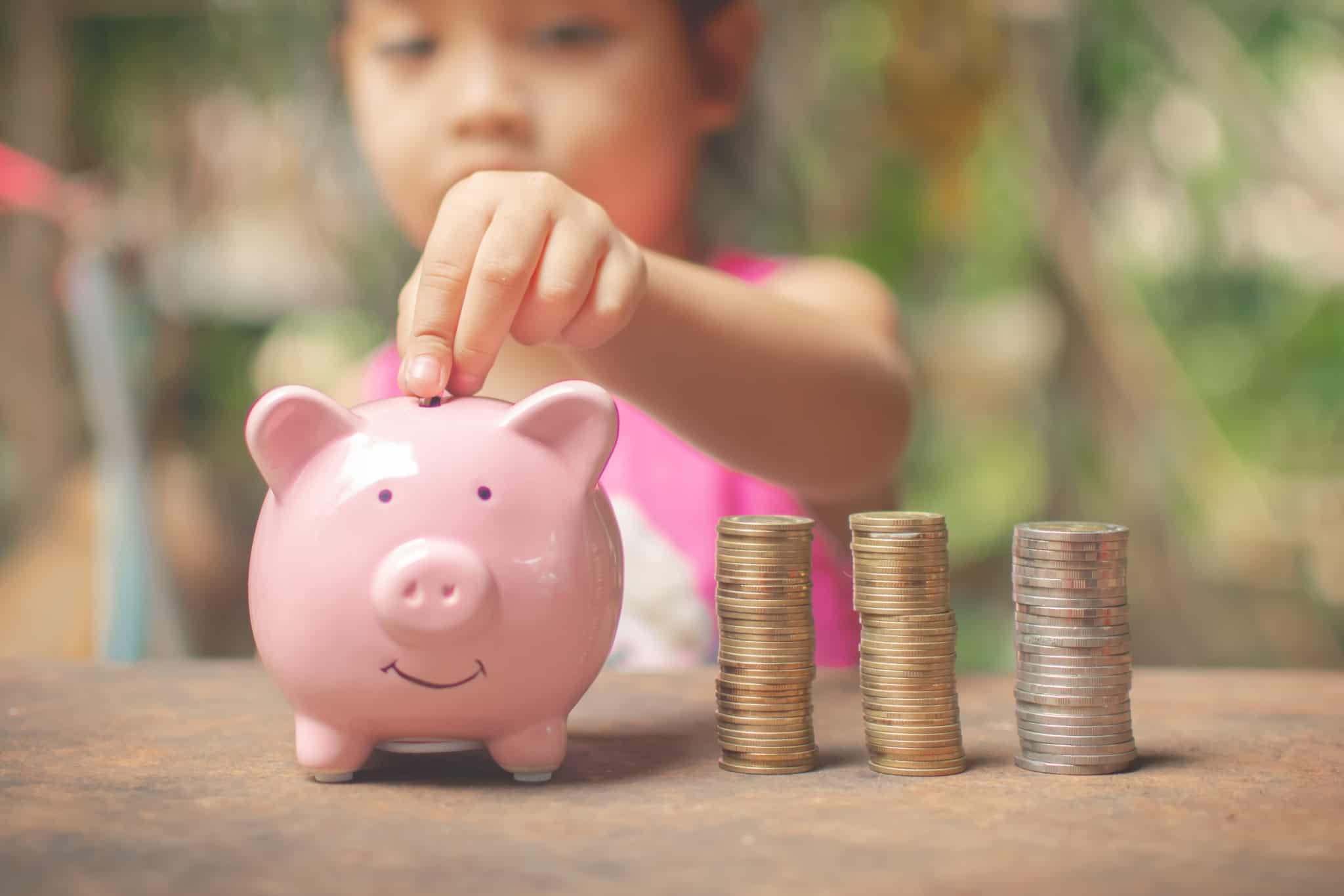 criança a colocar moedas num porquinho mealheiro cor de rosa