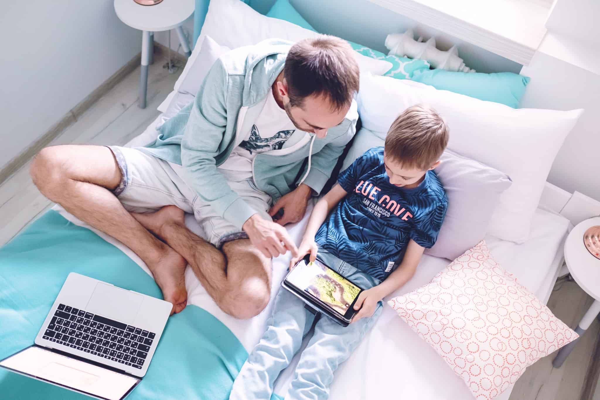 pai e filho sentados na cama a olhar para um tablet