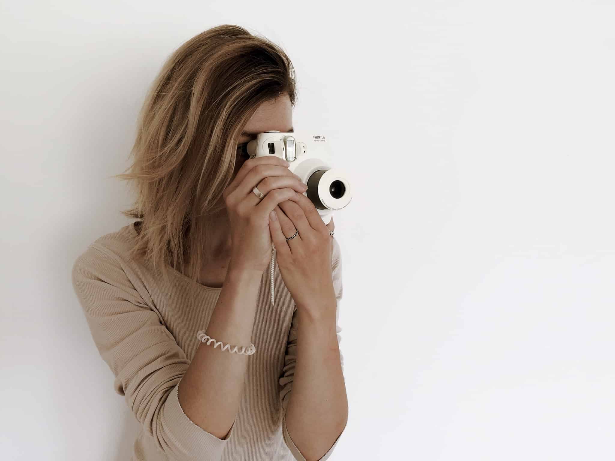 rapariga loira a tirar uma foto com camara branca