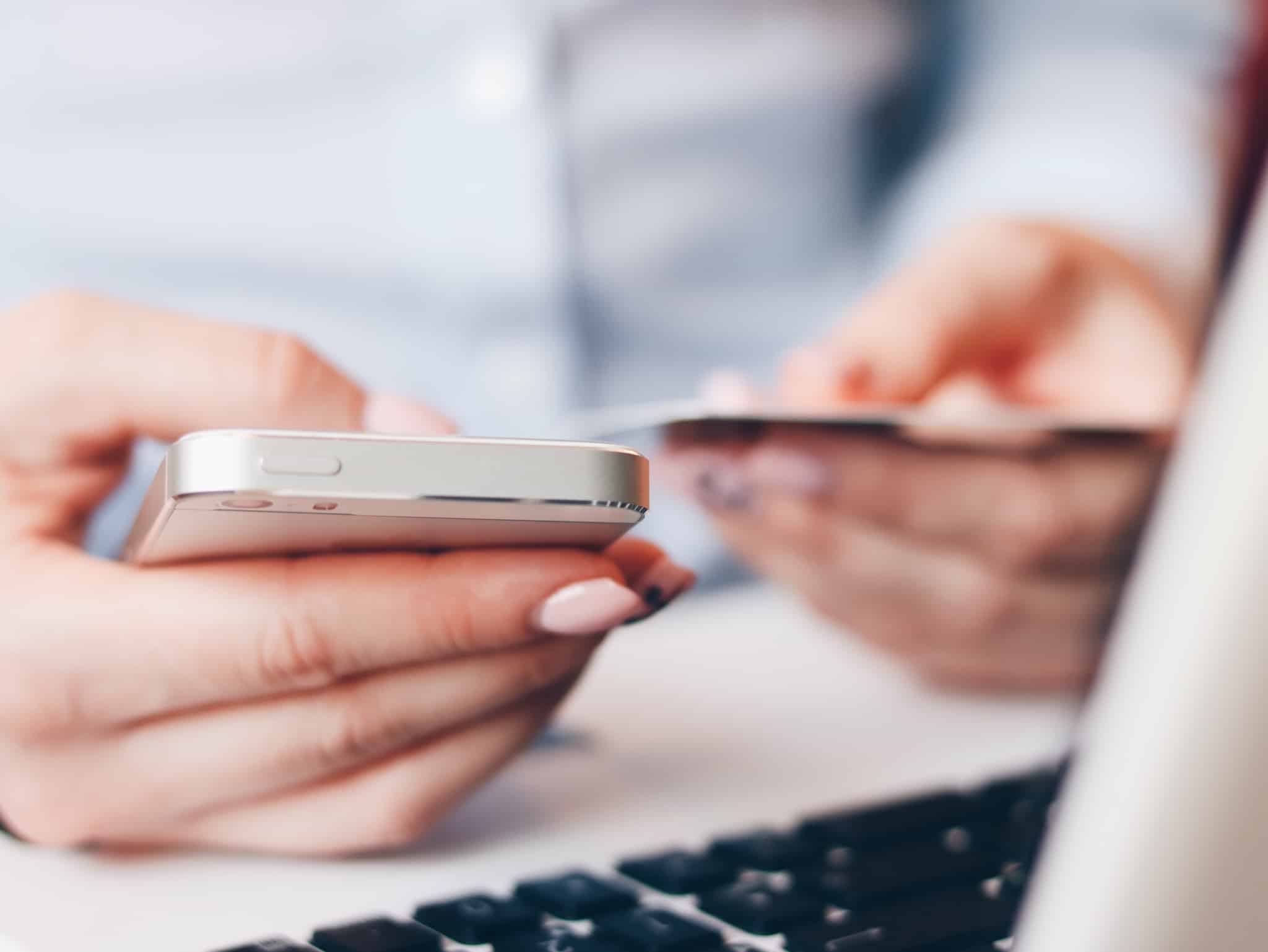 senhora com unhas rosa a segurar o telemóvel e um cartão de pagamentos