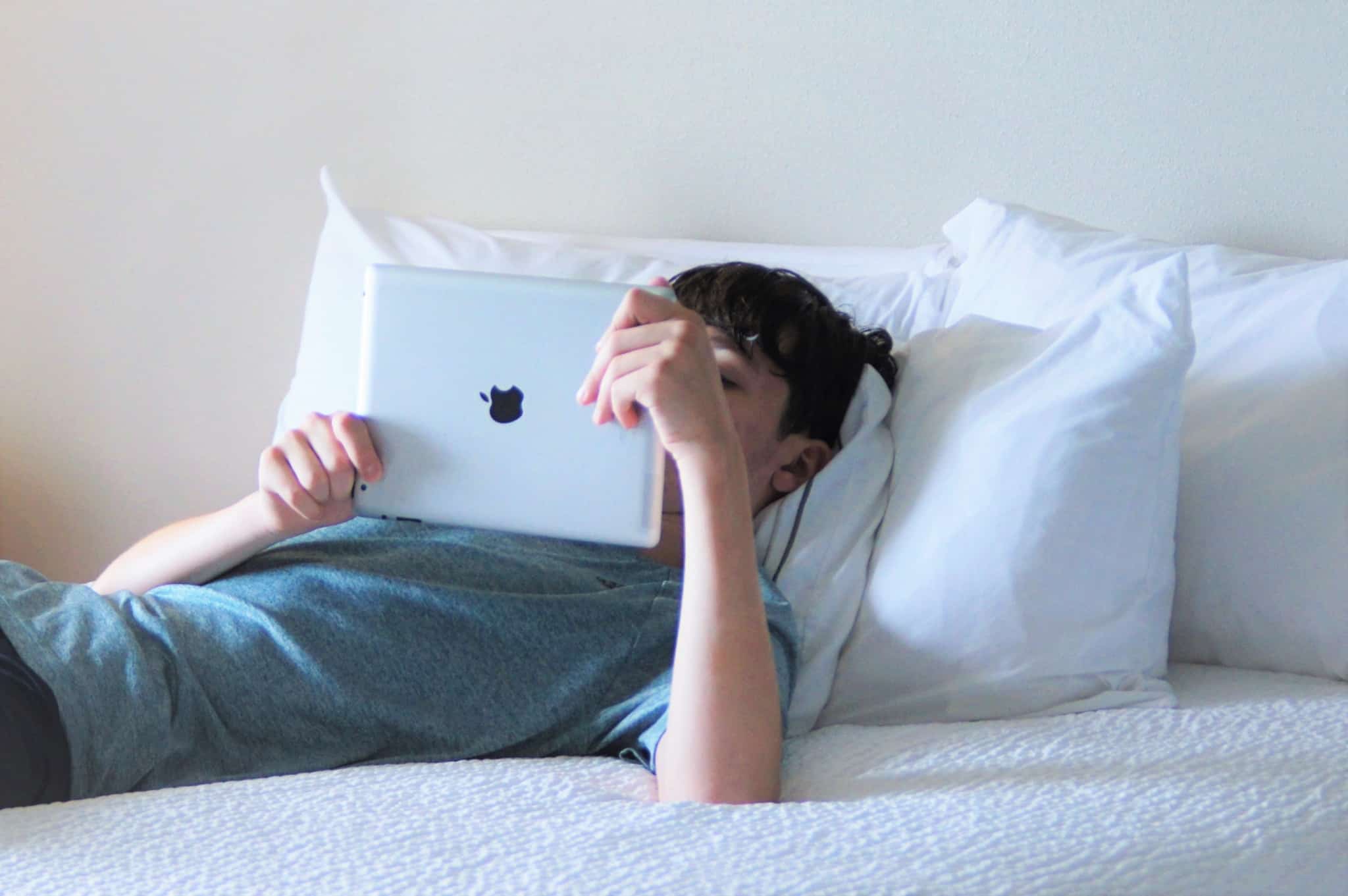 adolescente com um ipad na mao deitado na cama