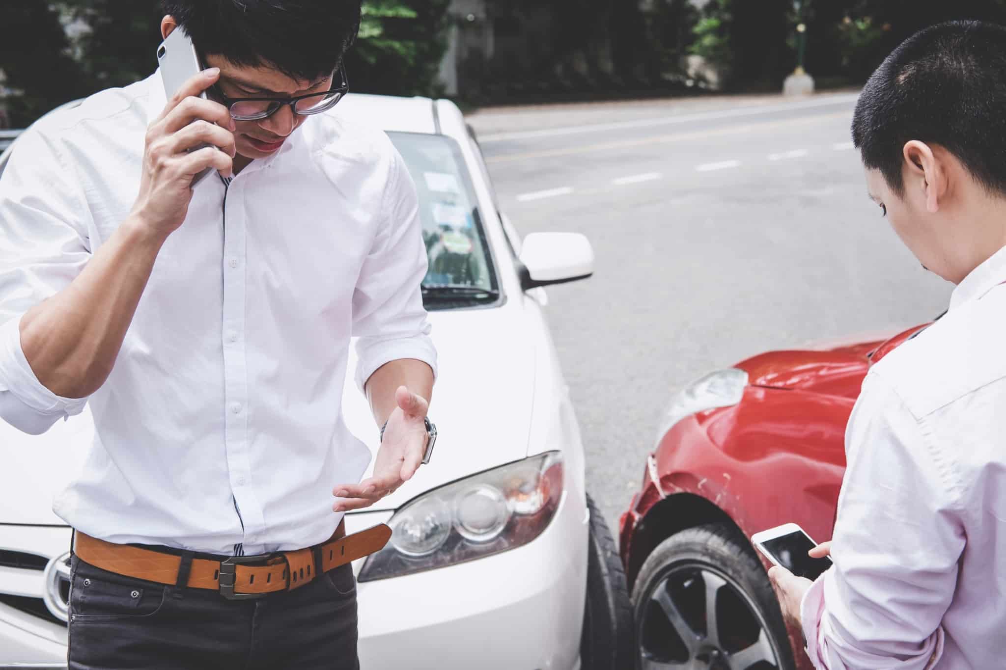 homem a falar ao telemóvel depois de ter um acidente automóvel