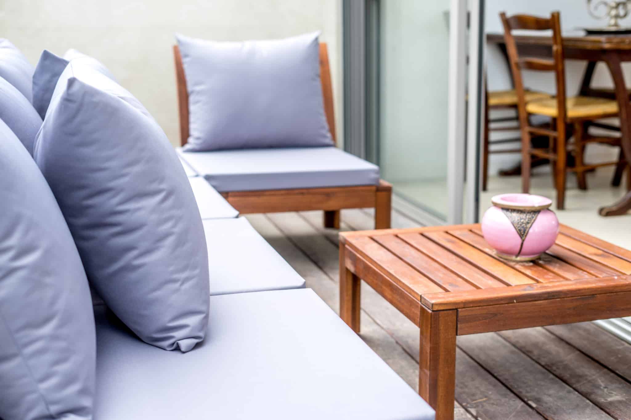 terraço exterior com almofadas e mesa quadrada de madeira com um cinzeiro cor de rosa