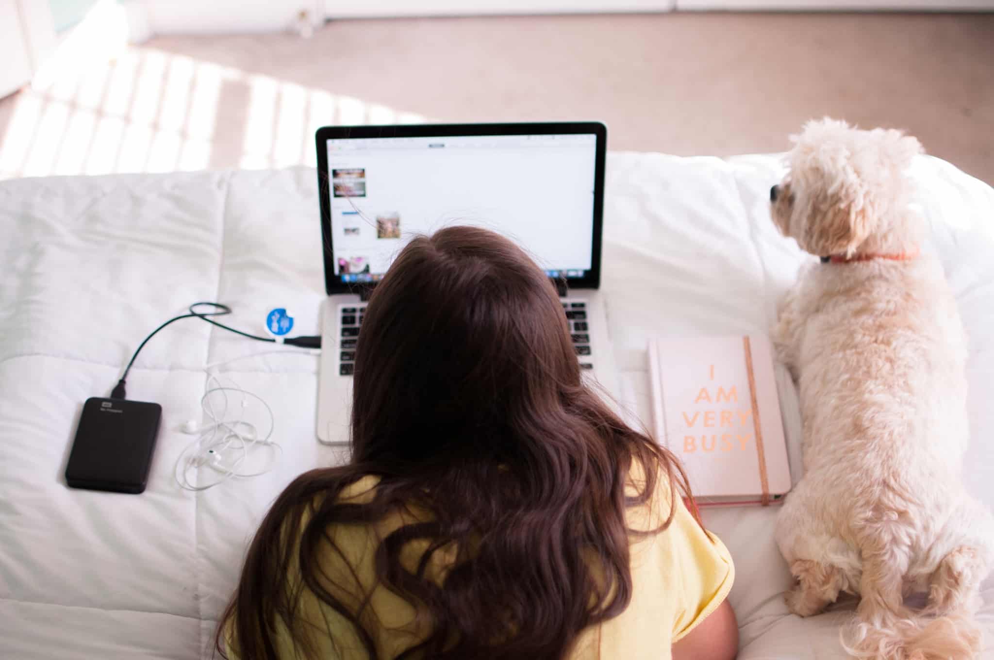 rapariga deitada na cama com o computador aberto e o cão ao lado
