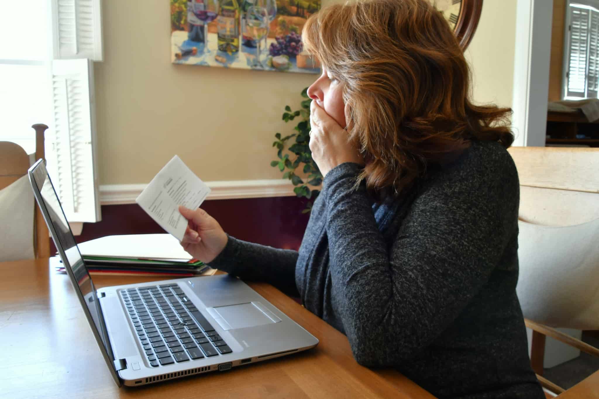 senhora com o computador à frente a olhar preocupada para uma carta