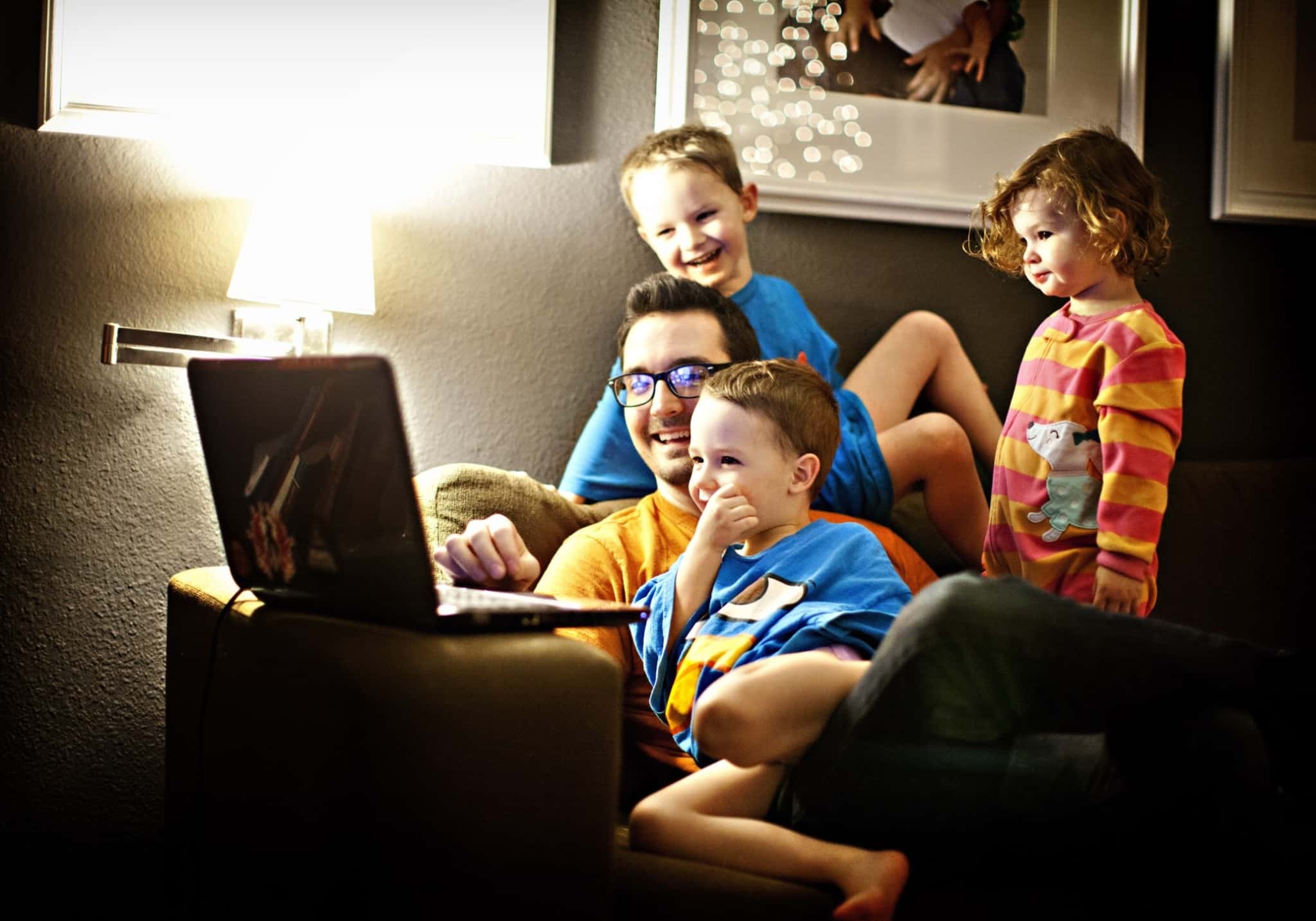 Pai com três filhos no sofá a ver o computador