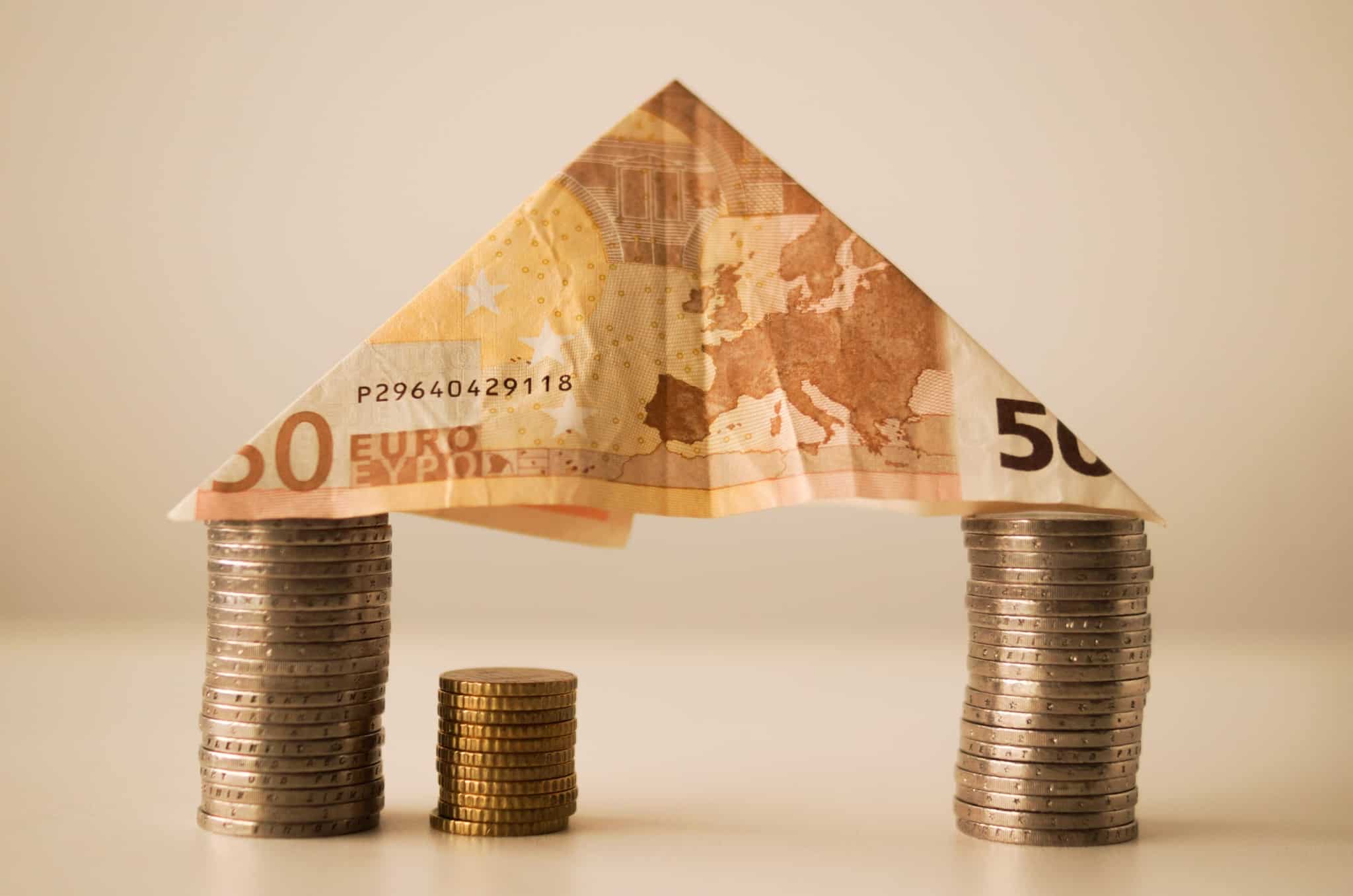 Imagem de uma casa feita com pilhas de moedas com uma nota de 50 euros em cima