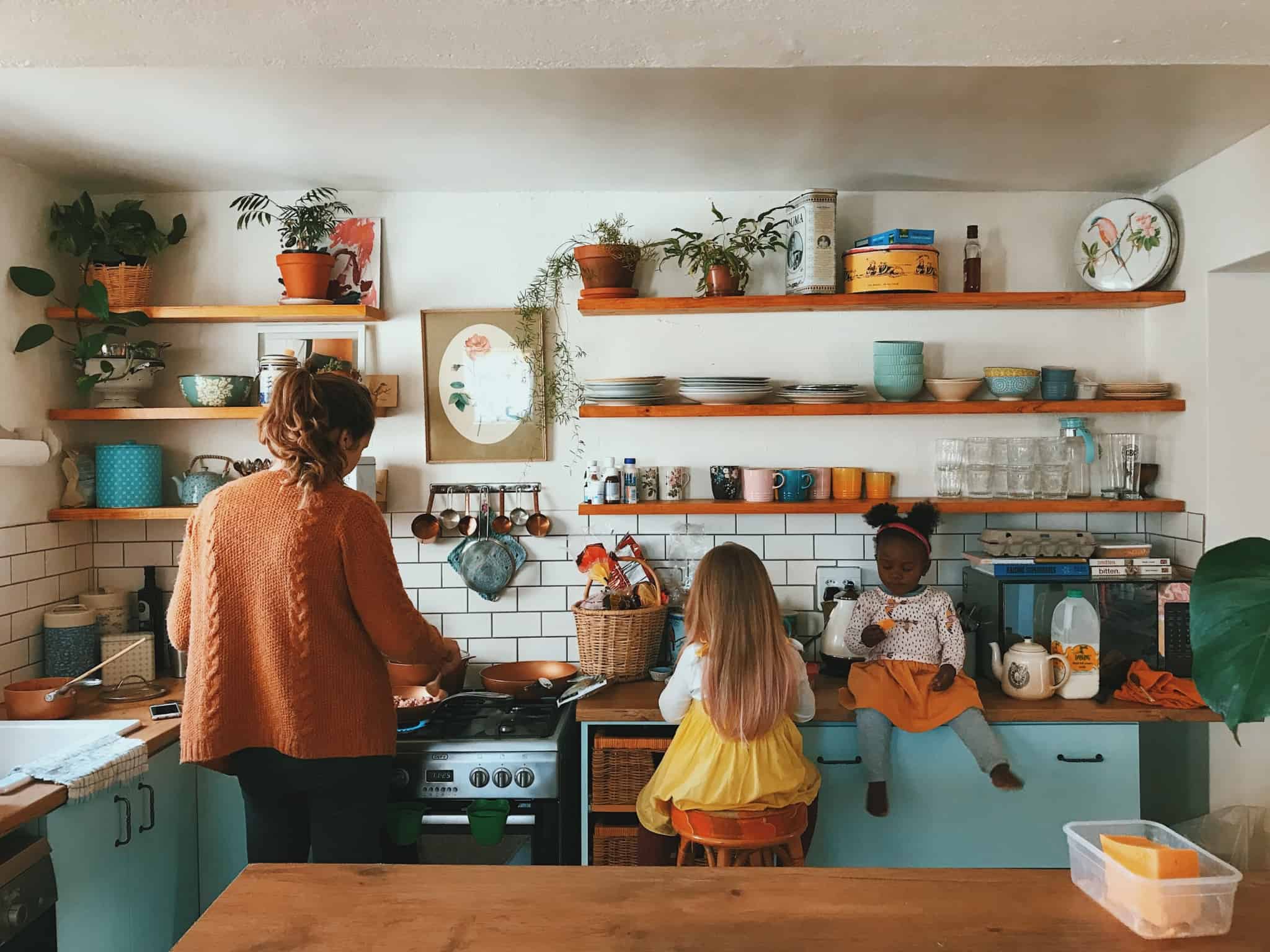 mãe a cozinhar com as duas filhas sentadas ao lado
