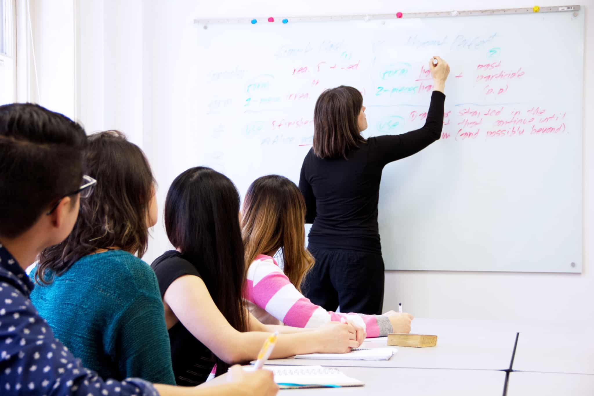professora a escrever num quadro branco com 4 alunos a ver