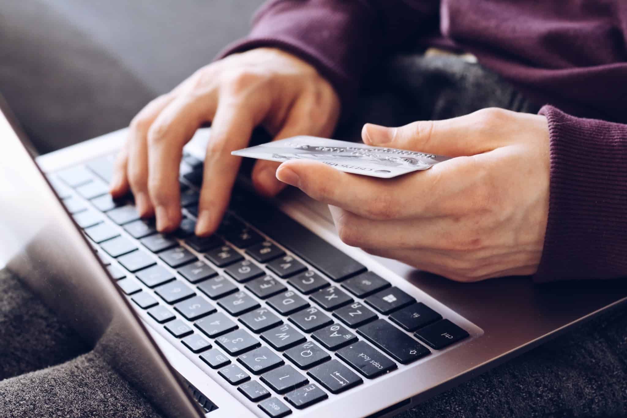 homem a fazer compras no computador e a segurar o cartão de pagamentos