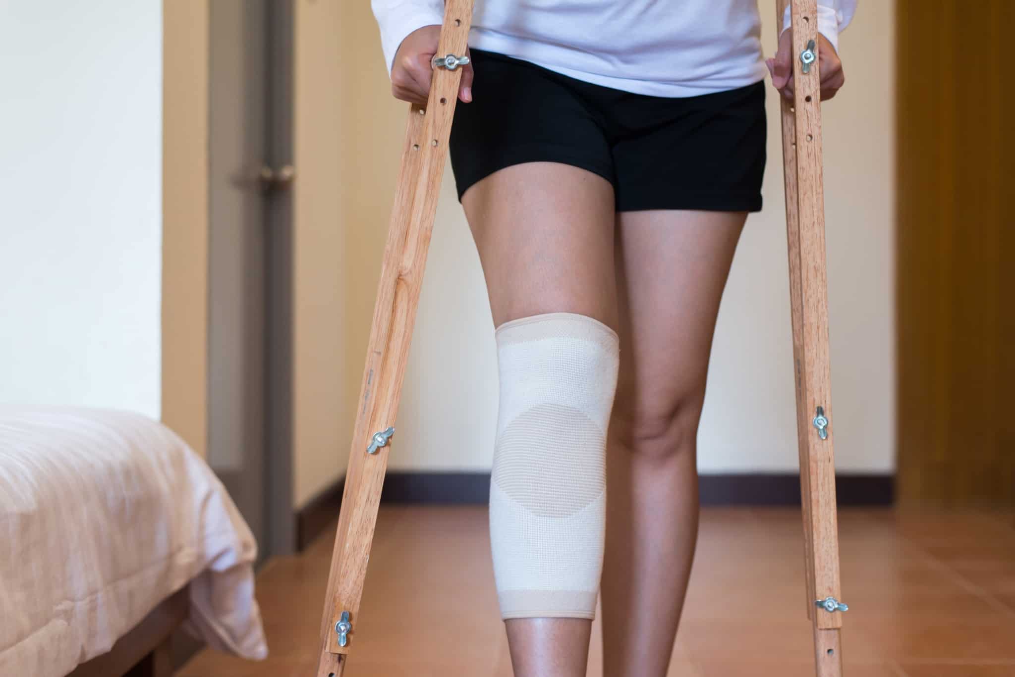 rapariga com um penso grande na perna e a andar de muletas de madeira