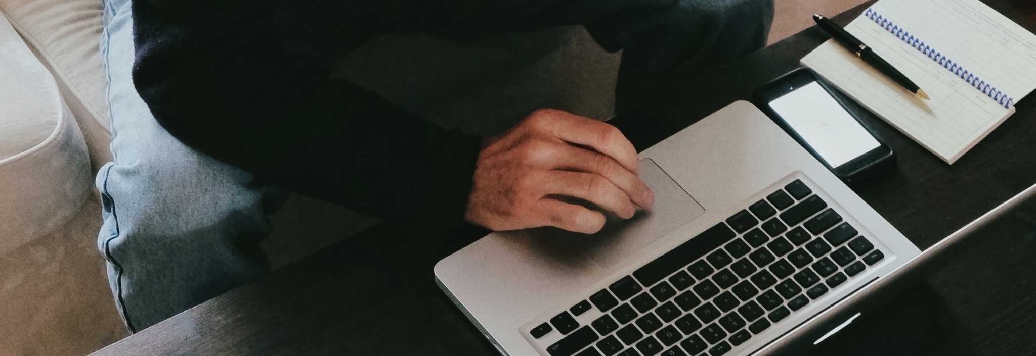 Homem em frente ao computador e com um bloco e uma caneta ao seu lado.