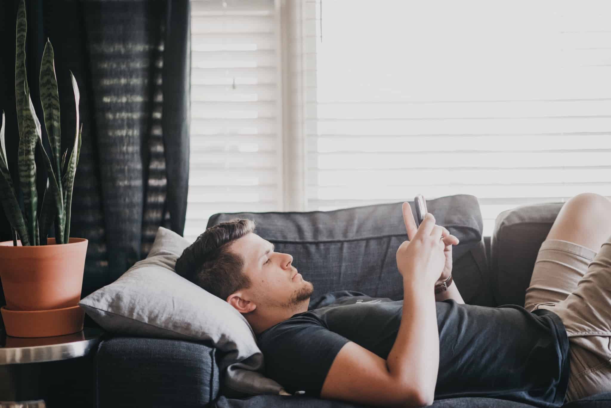 homem deitado no sofá a mexer no telemóvel
