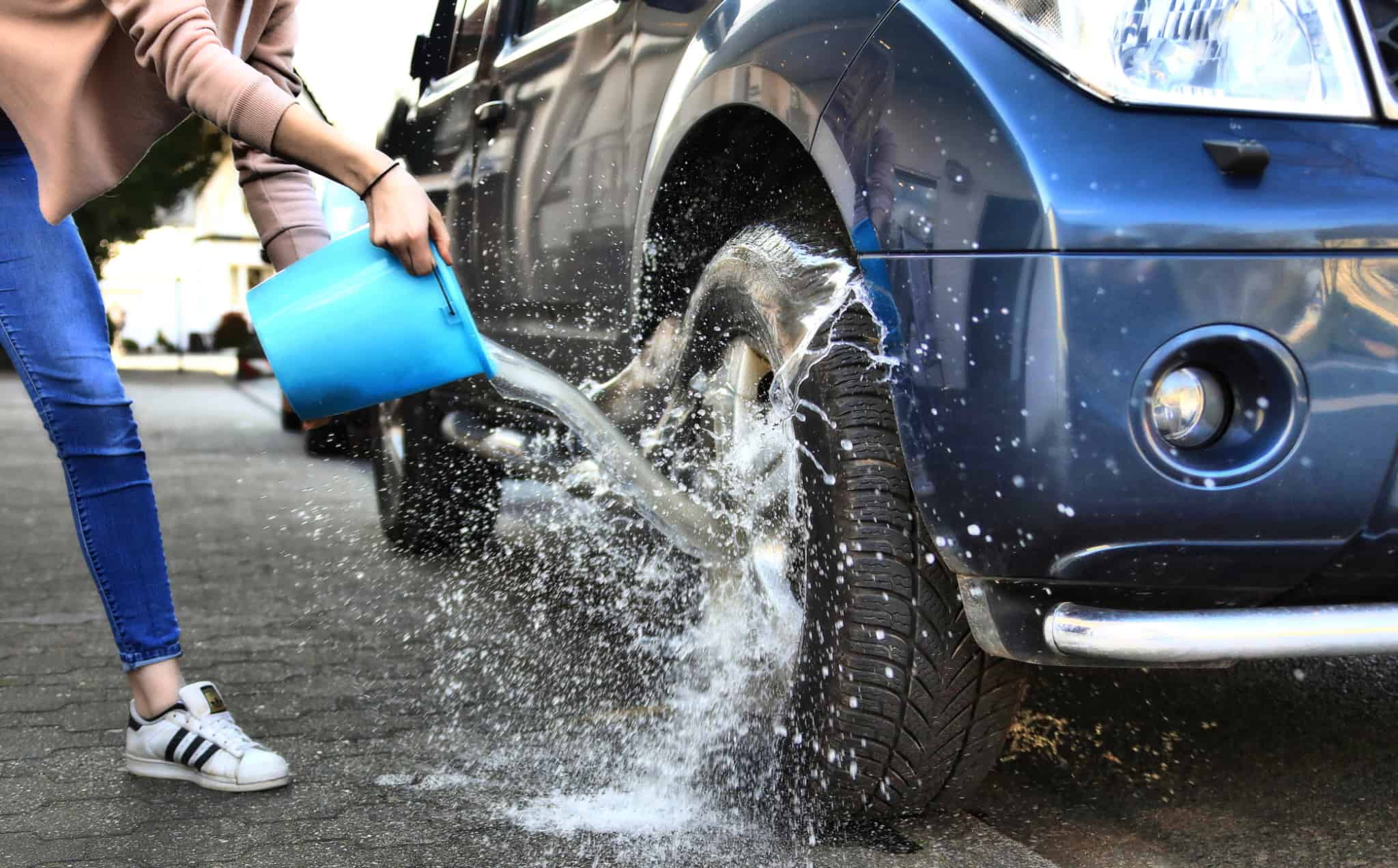 pessoa a atirar um balde de água para o pneu de um carro
