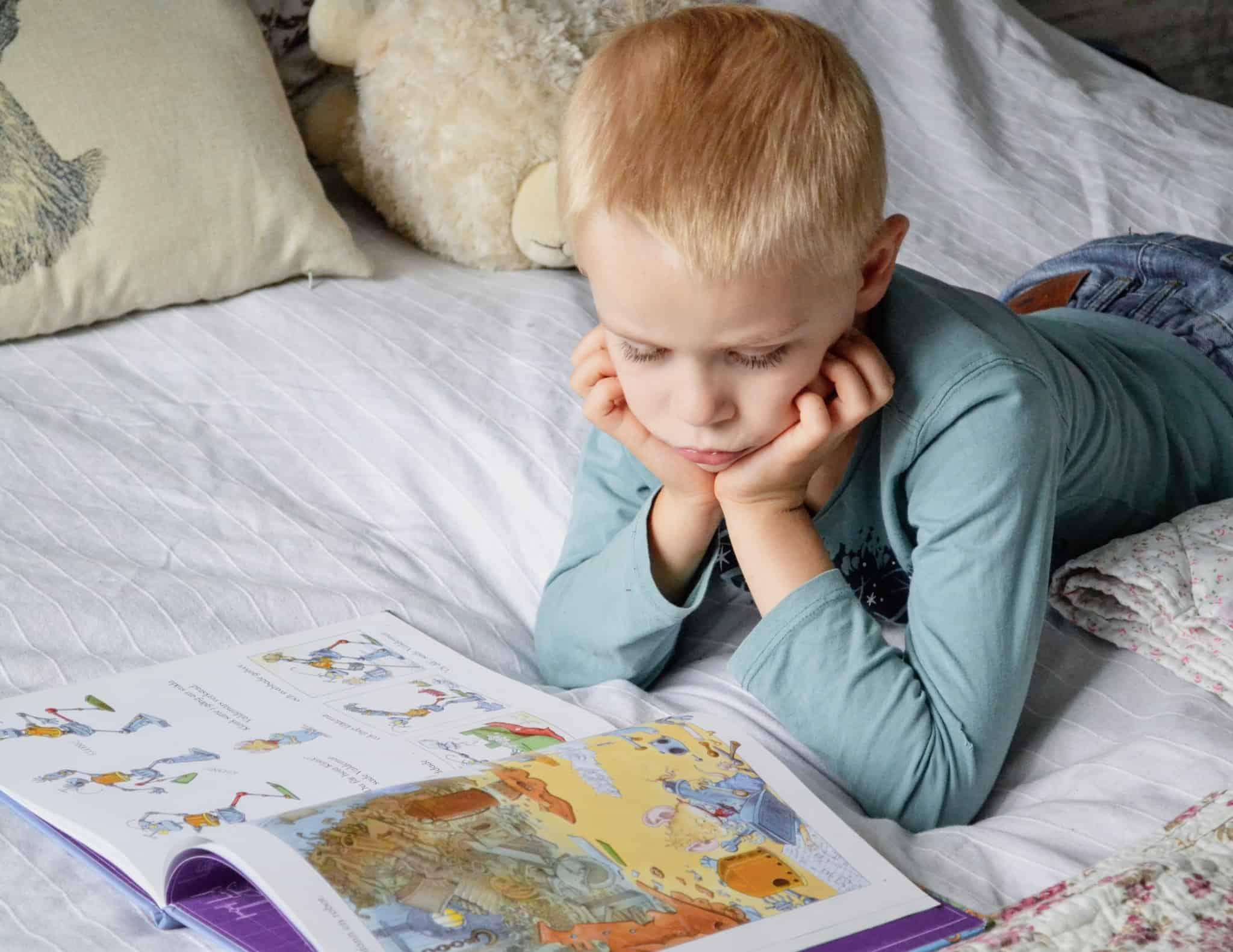 criança loira deitada na cama a ler um livro