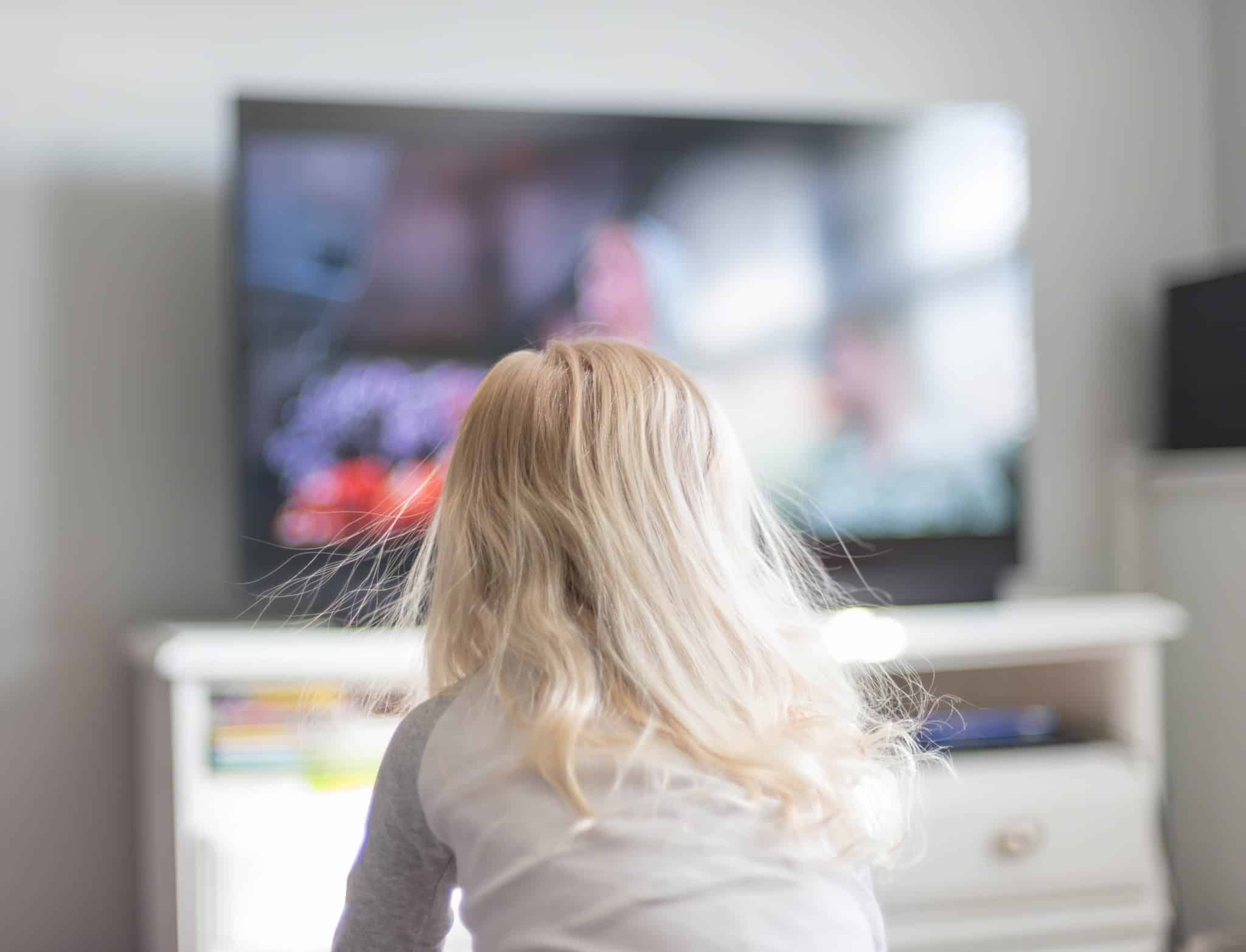 criança assiste à televisão, sentada no sofá de casa