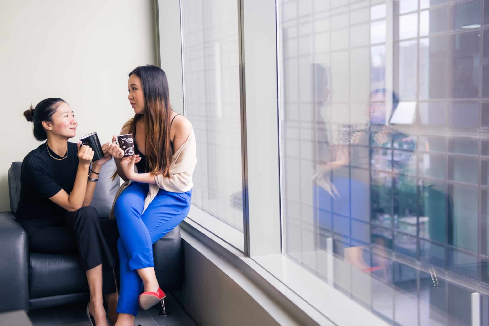 duas colegas de trabalho a falar sentadas e a segurar chávenas de café