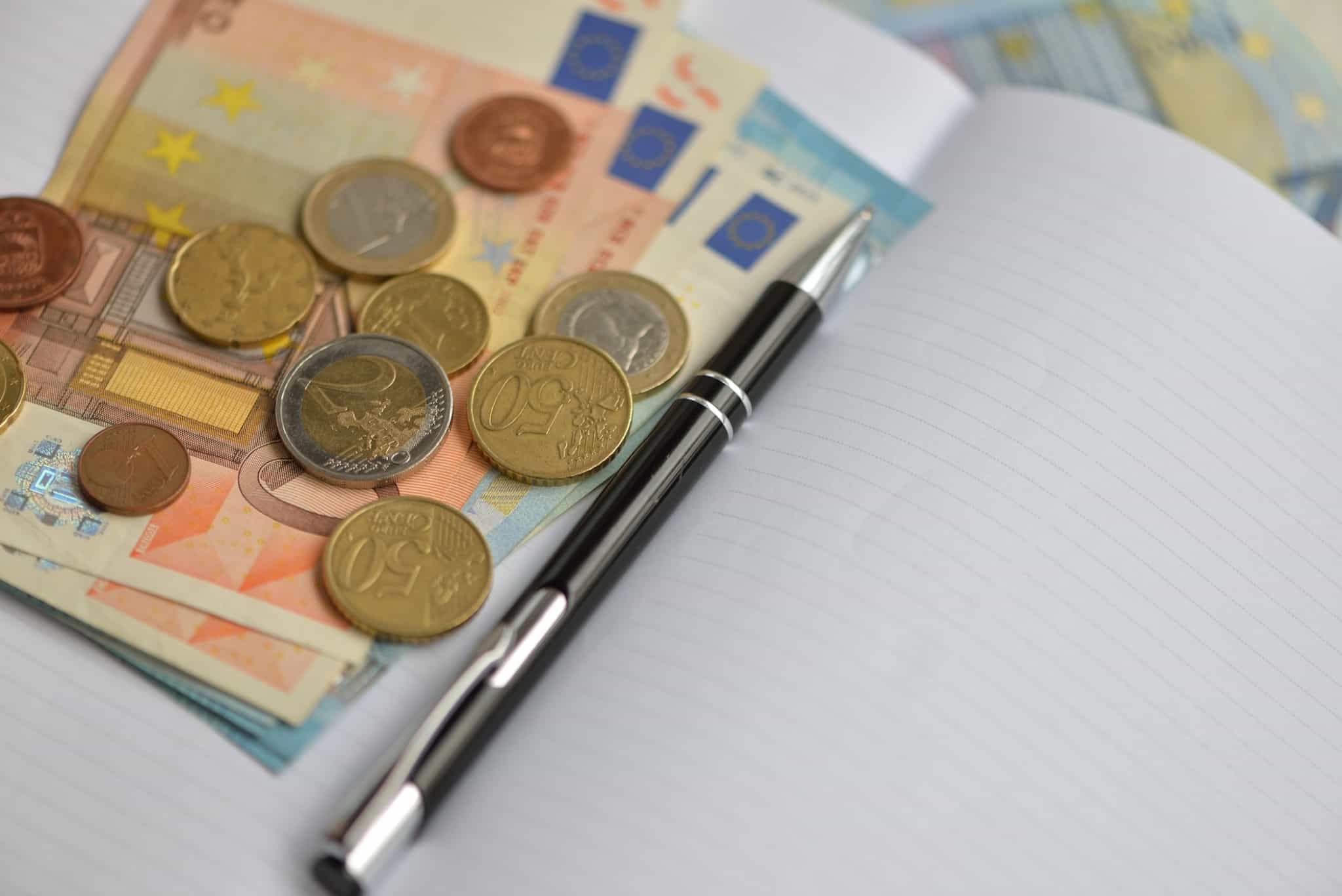 Notas e moedas de euro ao lado de um caneta