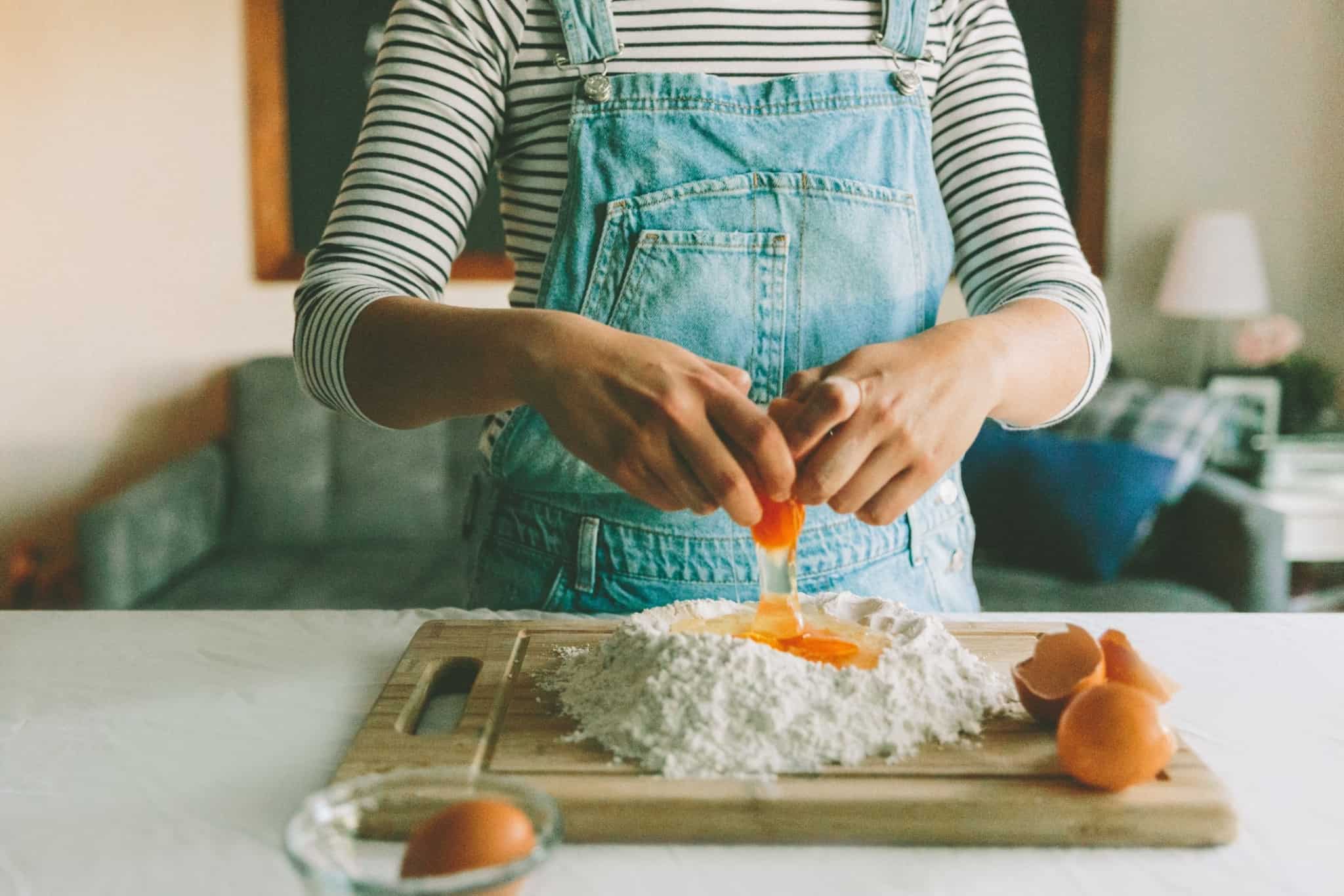 mulher a cozinhar e a partir um ovo em cima de farinha