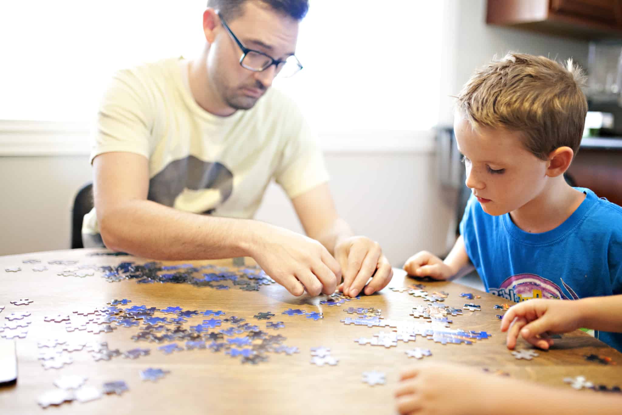 pai a fazer um puzzle em cima da mesa com o filho ao lado