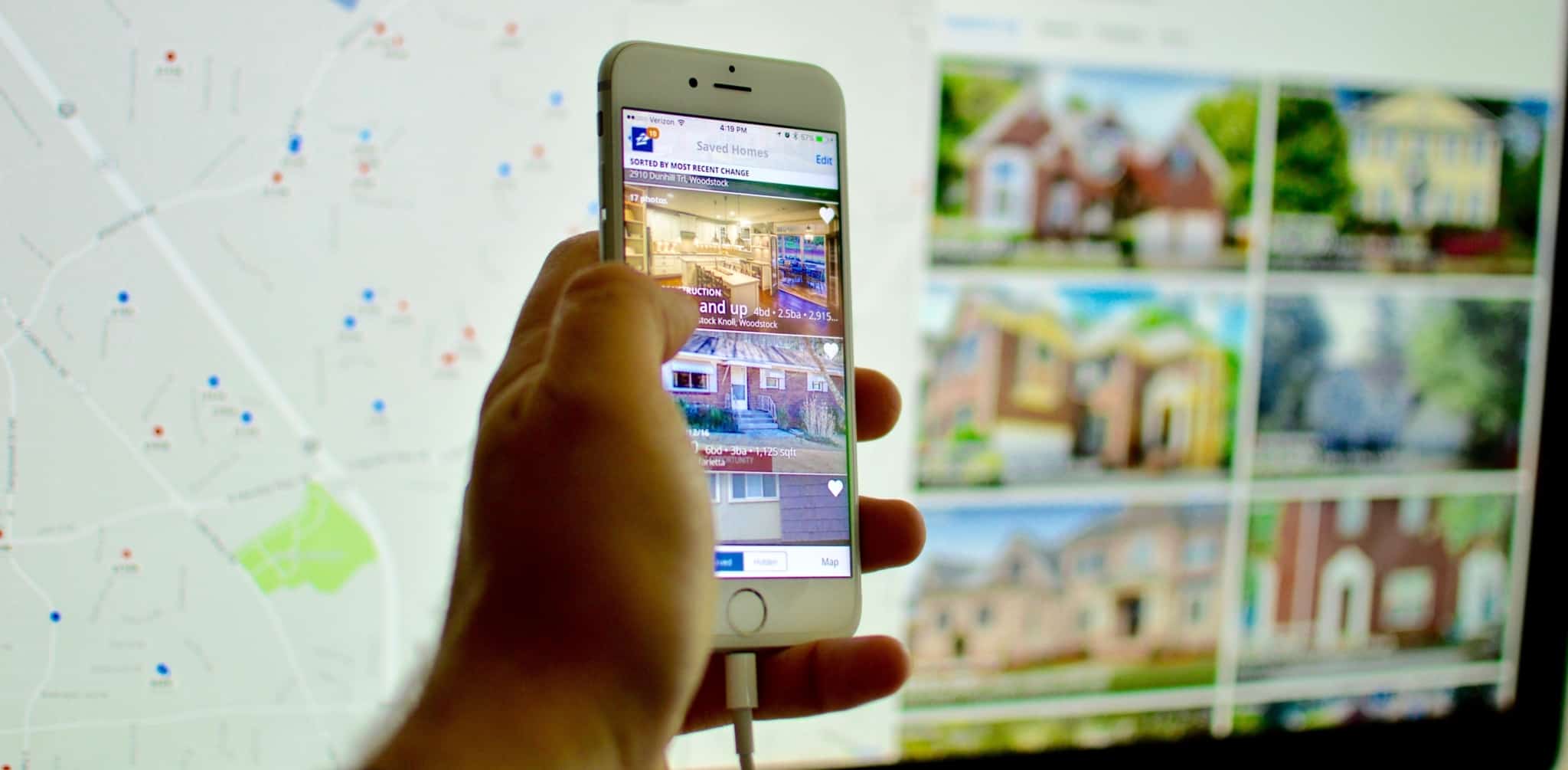 Uma mão a segurar um telemóvel com um portal de casas aberto