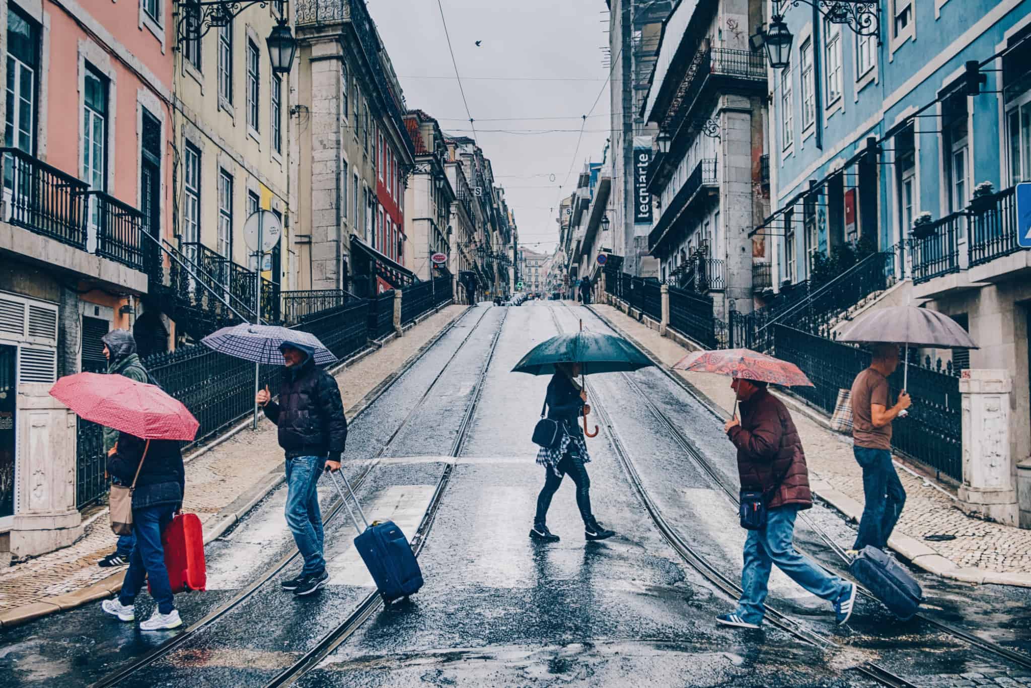 Pessoas a atravessarem uma rua de Lisboa, de chapéu de chuva