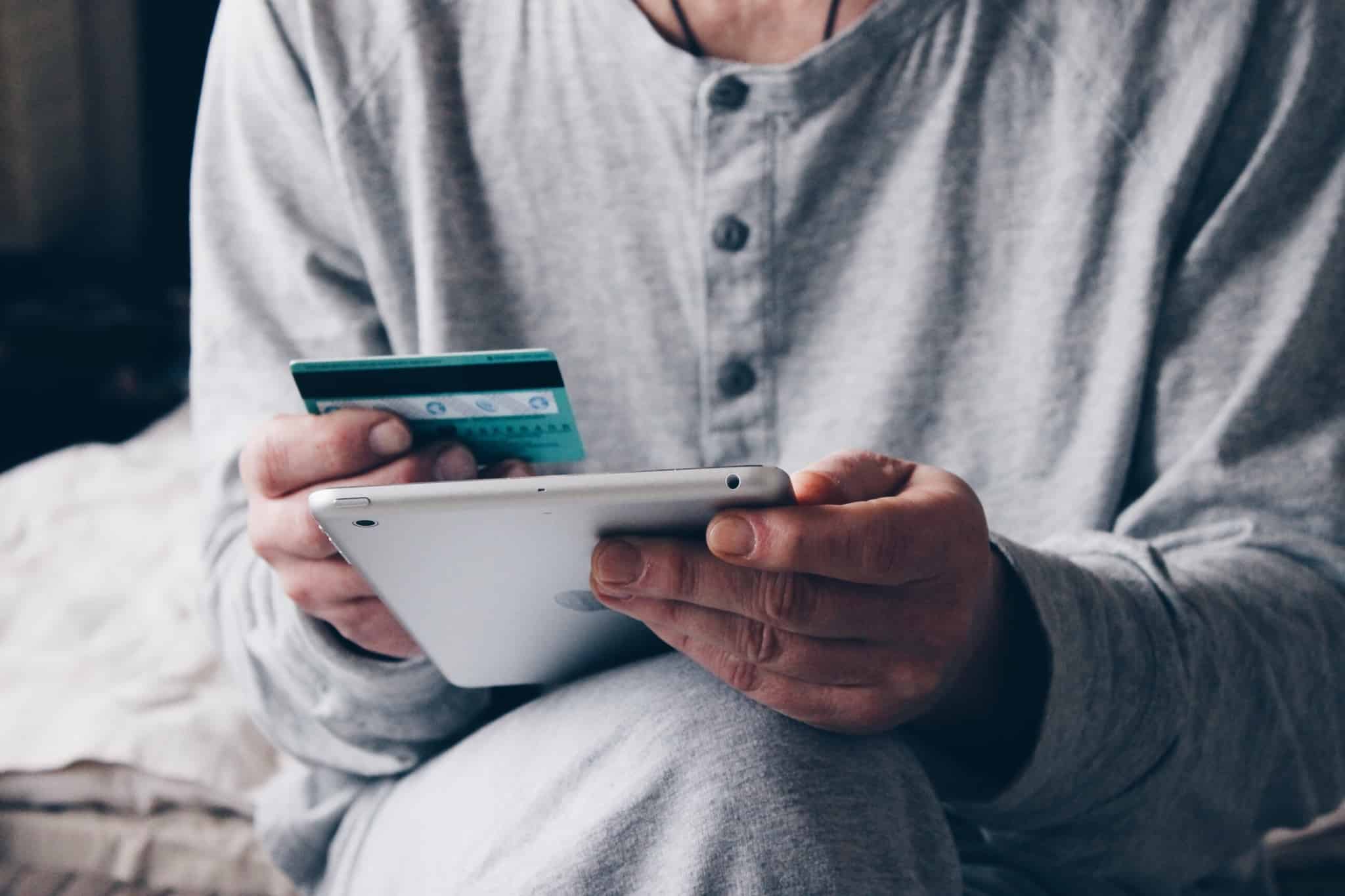 pessoa de pijama a segurar um tablet e o cartão de crédito