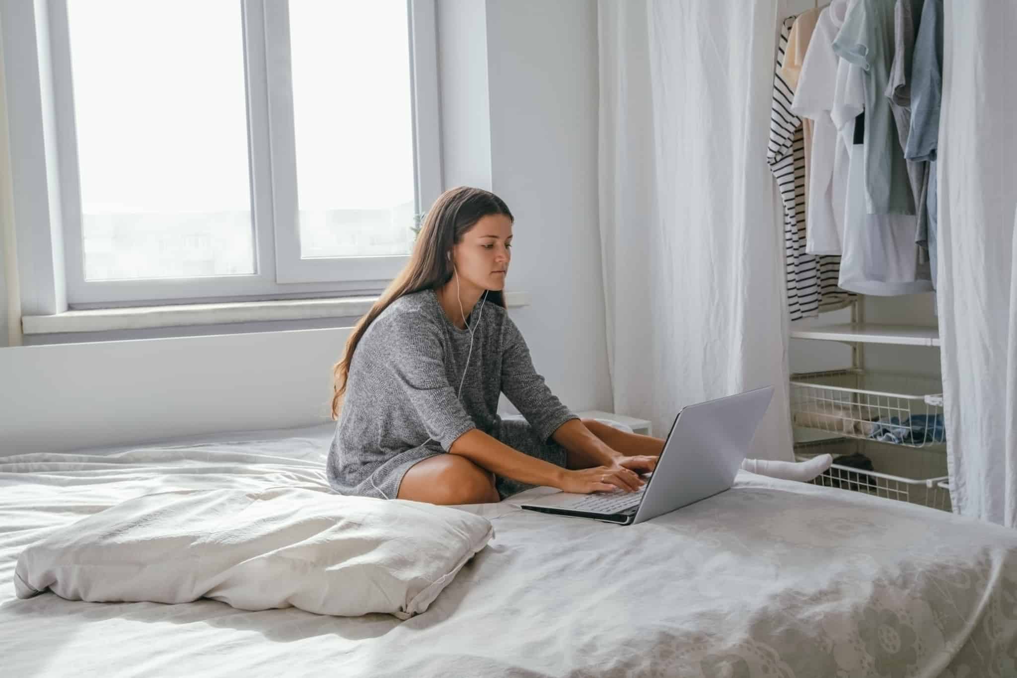 rapariga sentada na cama a escrever no computador