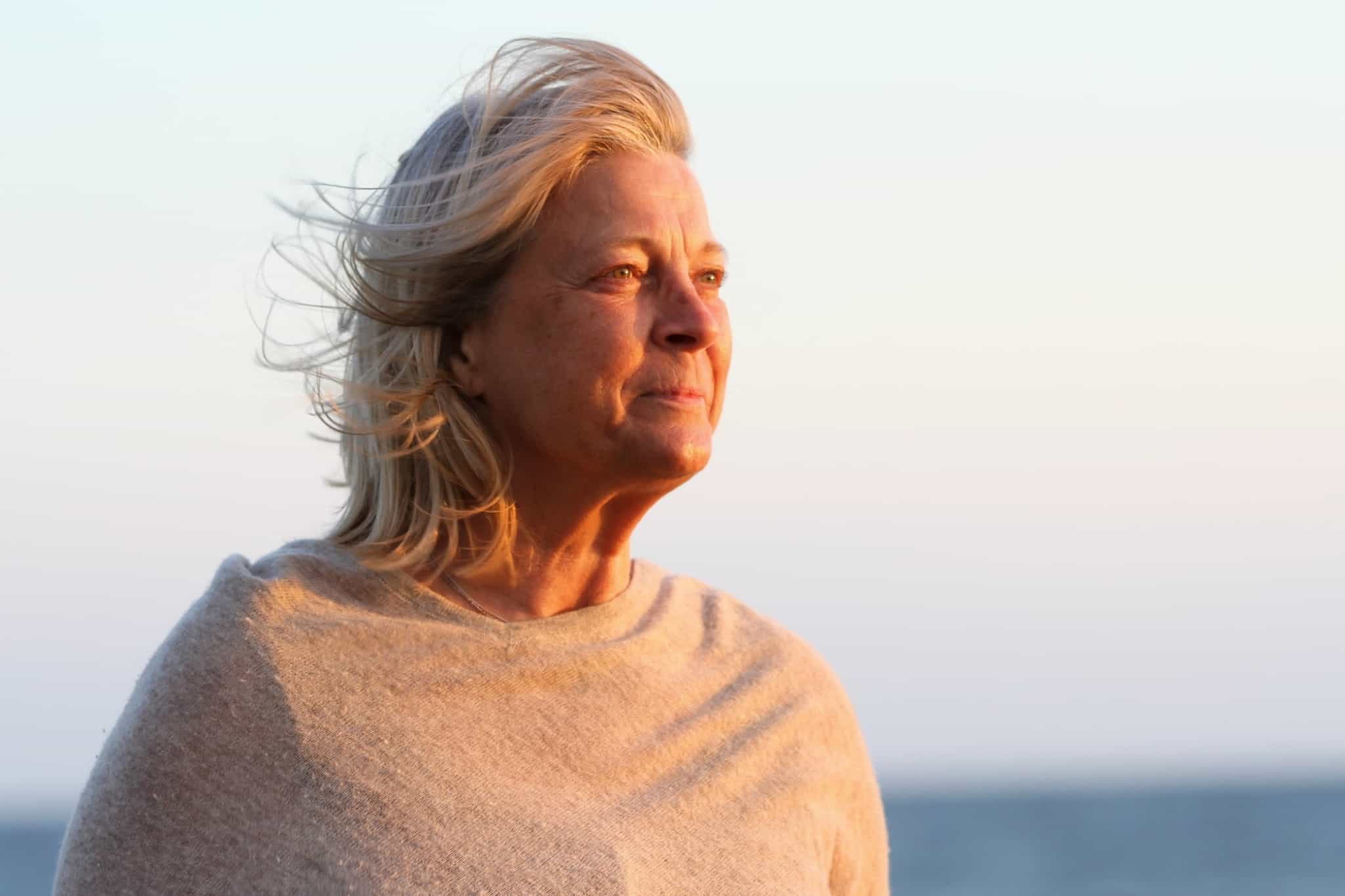 senhora com cabelo branco a olhar para o por do sol