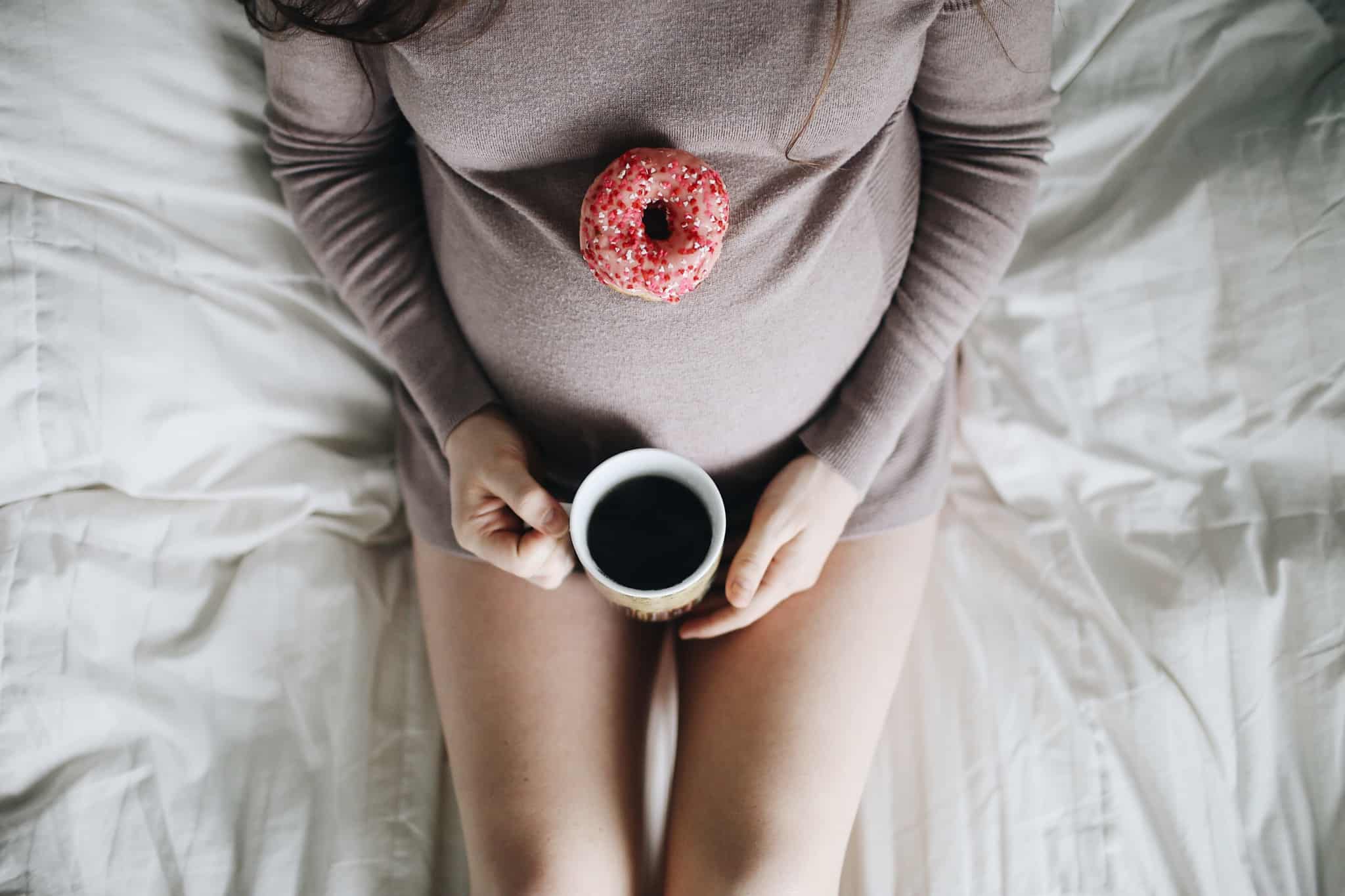 mulher grávida com caneta de café e donut em cima da barriga