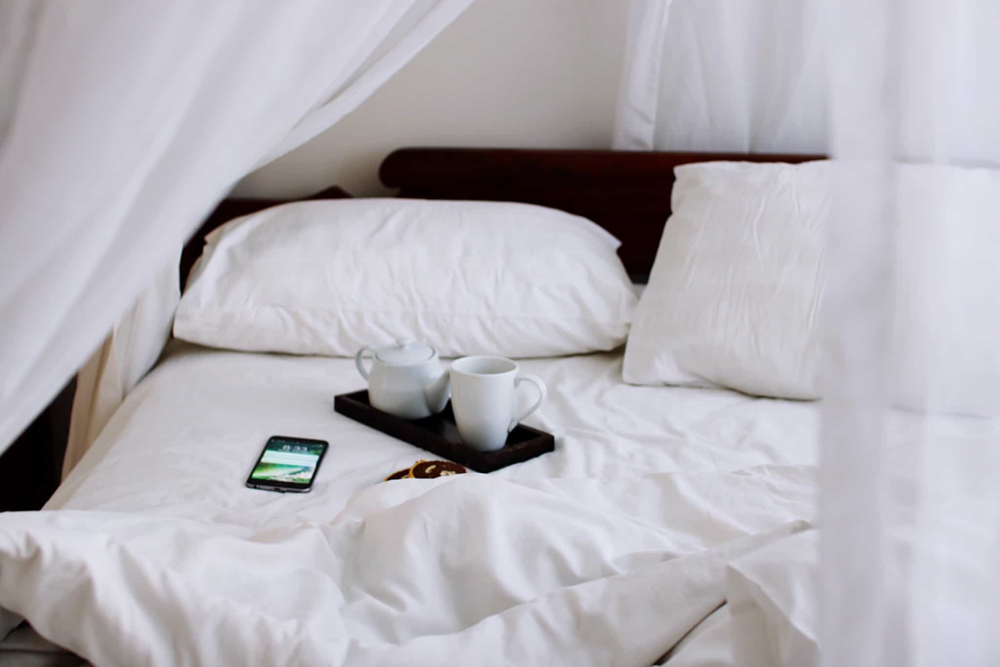 cama de hotel desfeita com tabuleiro e duas chávenas