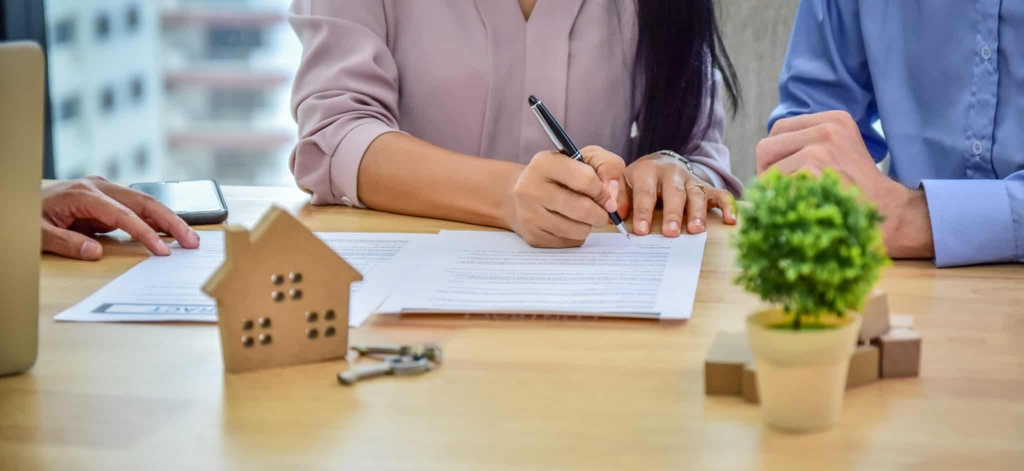 casal a assinar uns documentos com uma casa de madeira