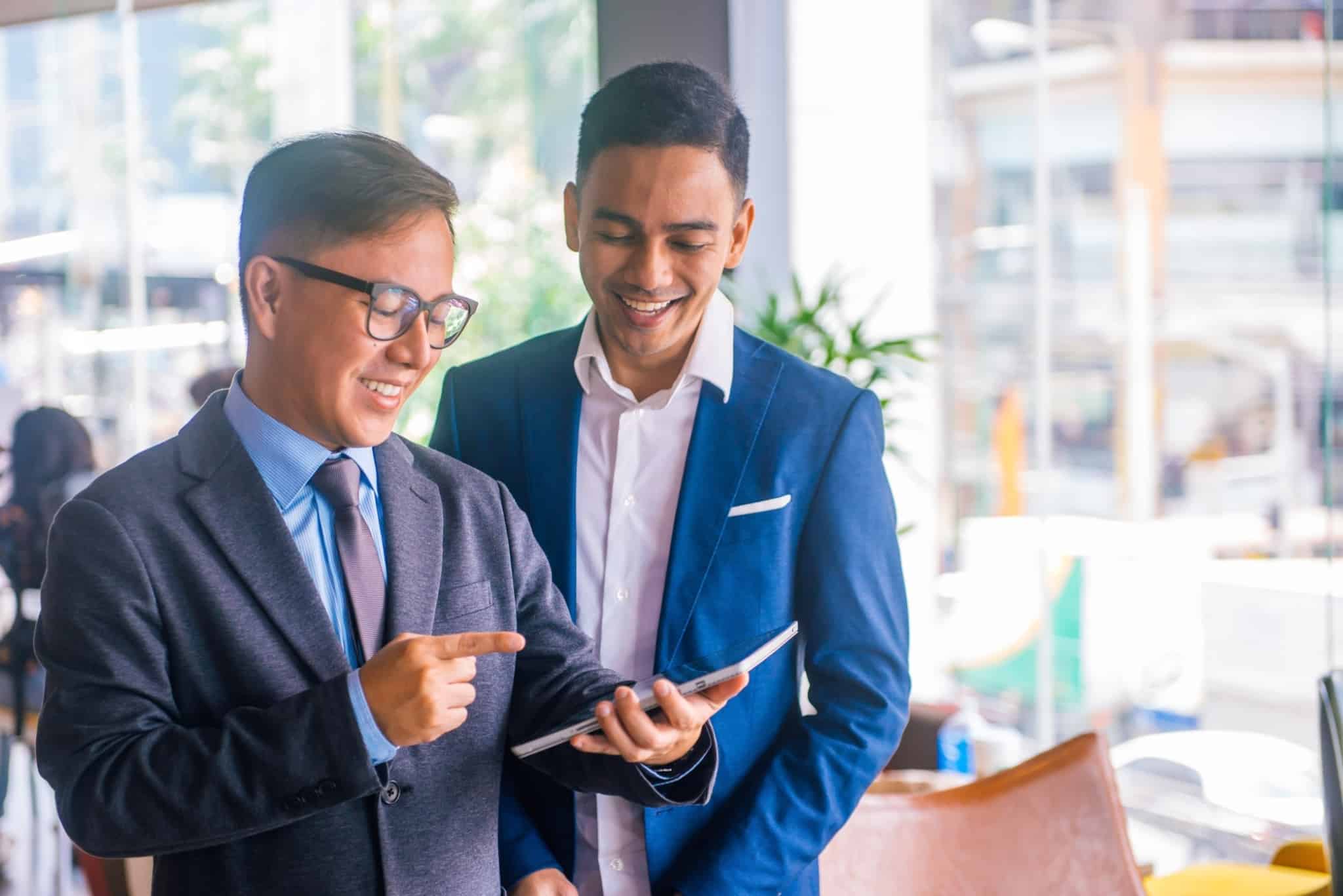 duas pessoas de fato a conversar e a olhar sorridentes para um tablet
