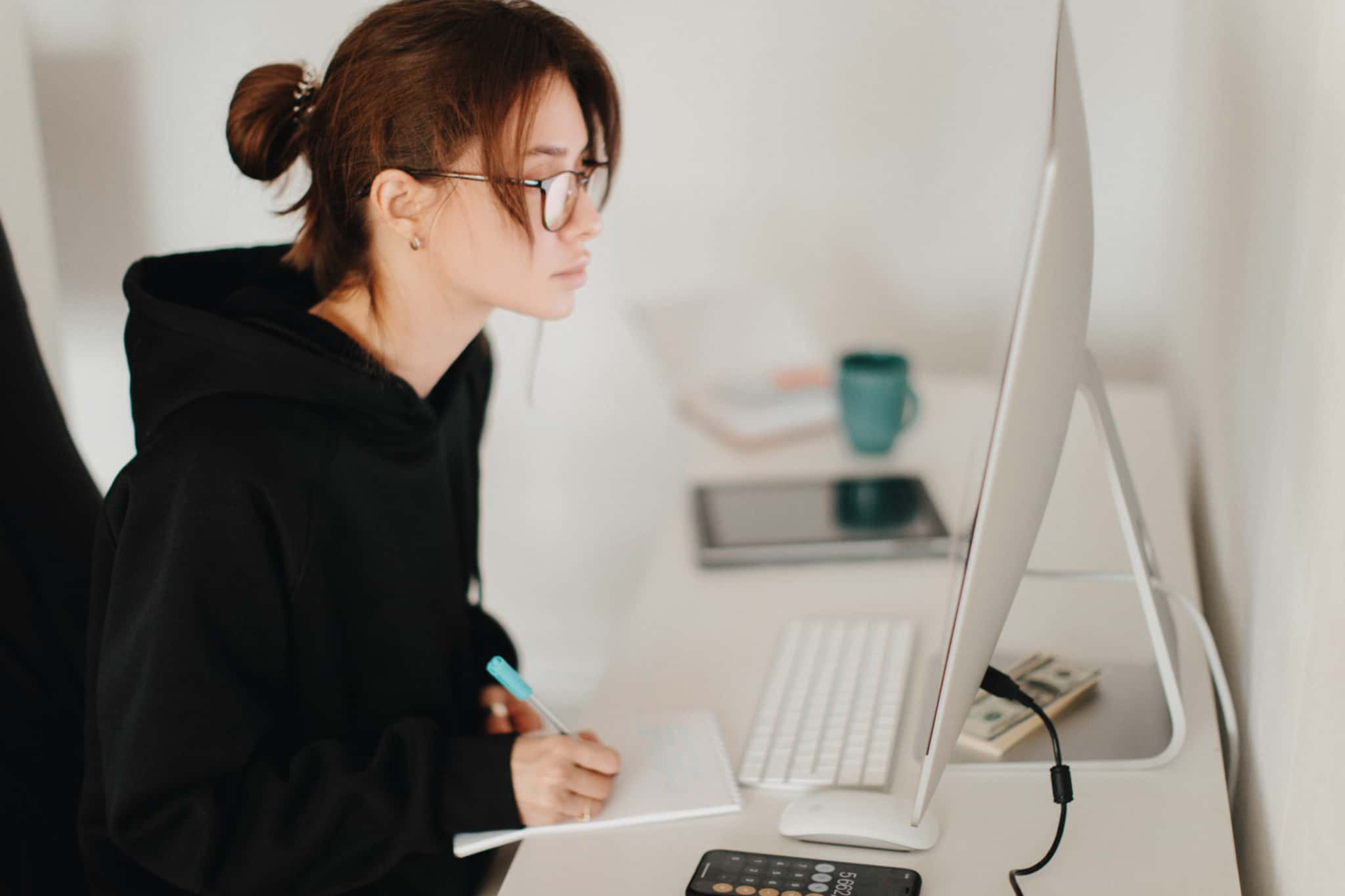 rapariga de cabelo apanhado e hoody preto a trabalhar à frente do monitor