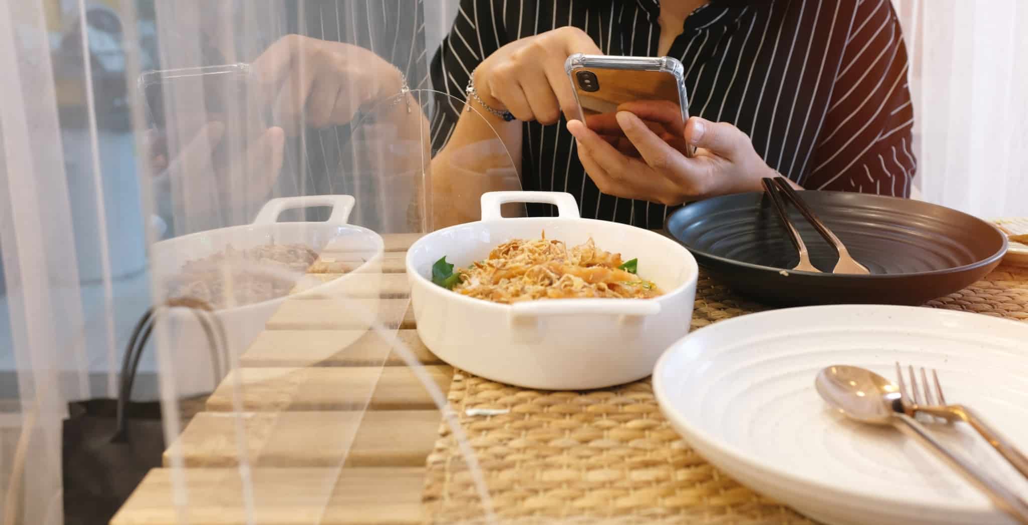 Mulher a comer num restaurante com um acrílico de proteção