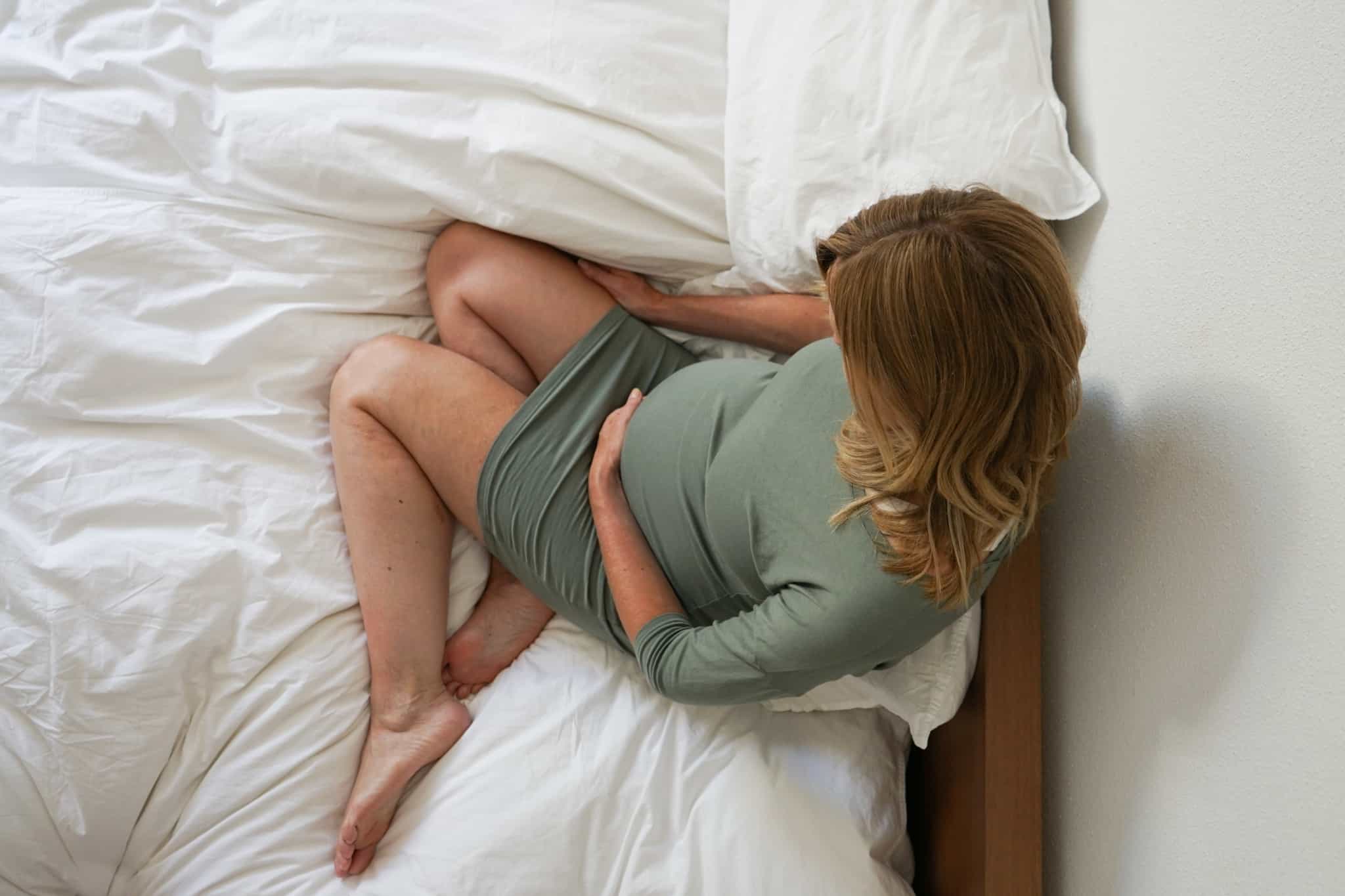 mulher grávida de vestido verde sentada em cima da cama