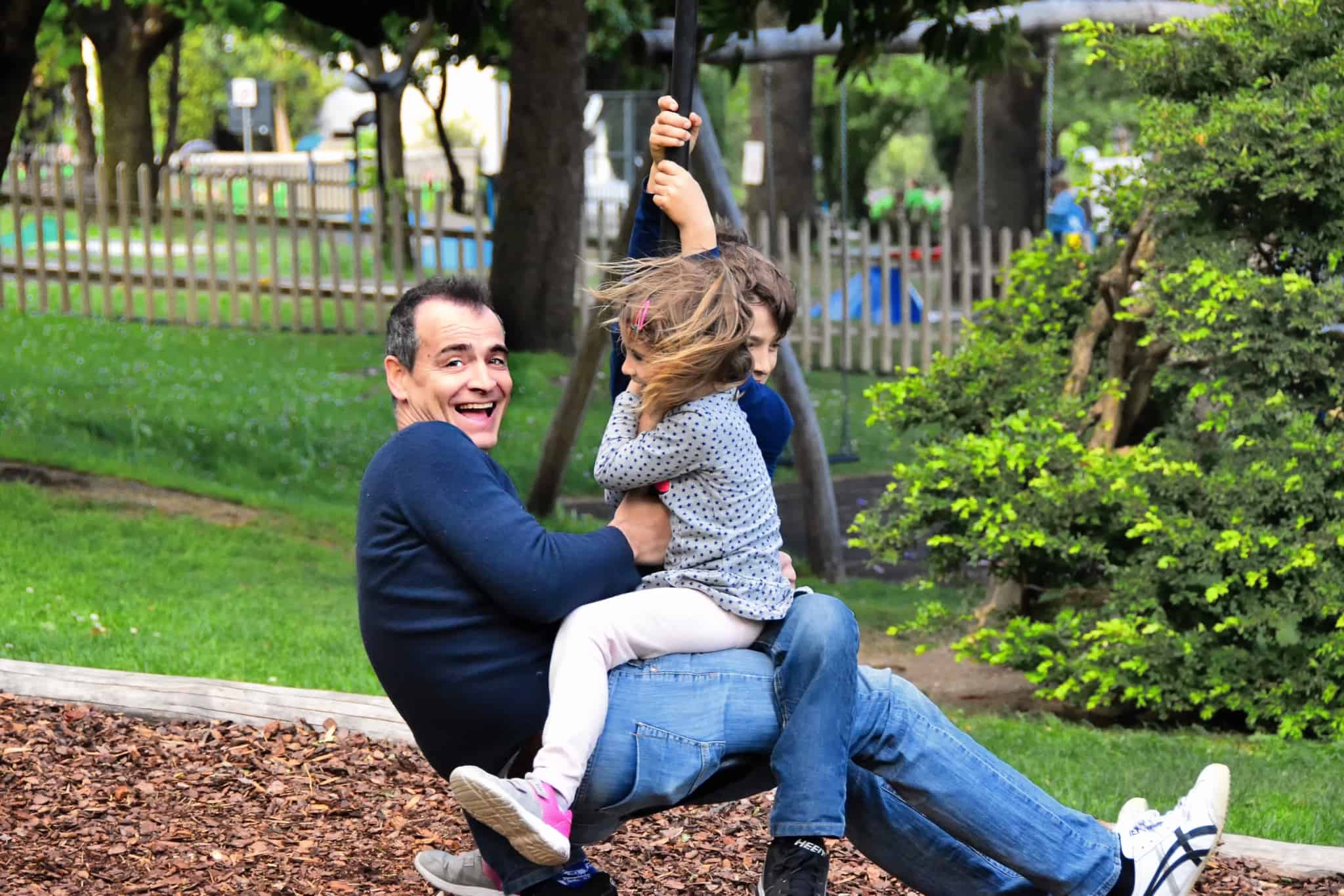 Pai com dois filhos num baloiço a divertirem-se